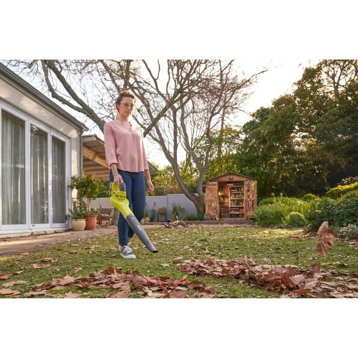 Una donna usa un soffiatore per foglie in giardino per pulire le foglie.
