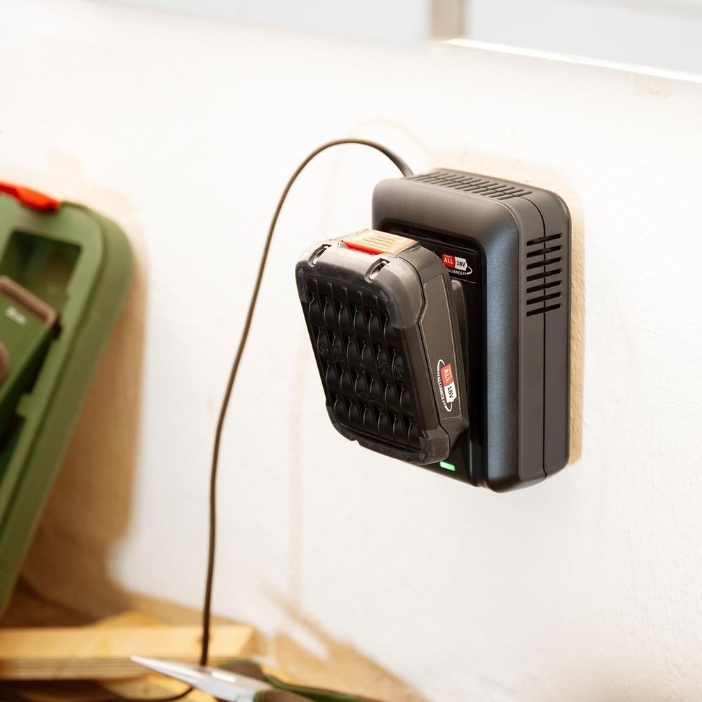 Un caricabatterie nero carica una batteria su un muro bianco.