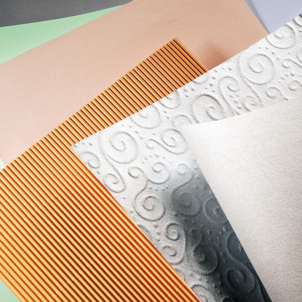 Plusieurs papiers superposés : ondulé, gaufré et lisse en rose, vert, gris et blanc.