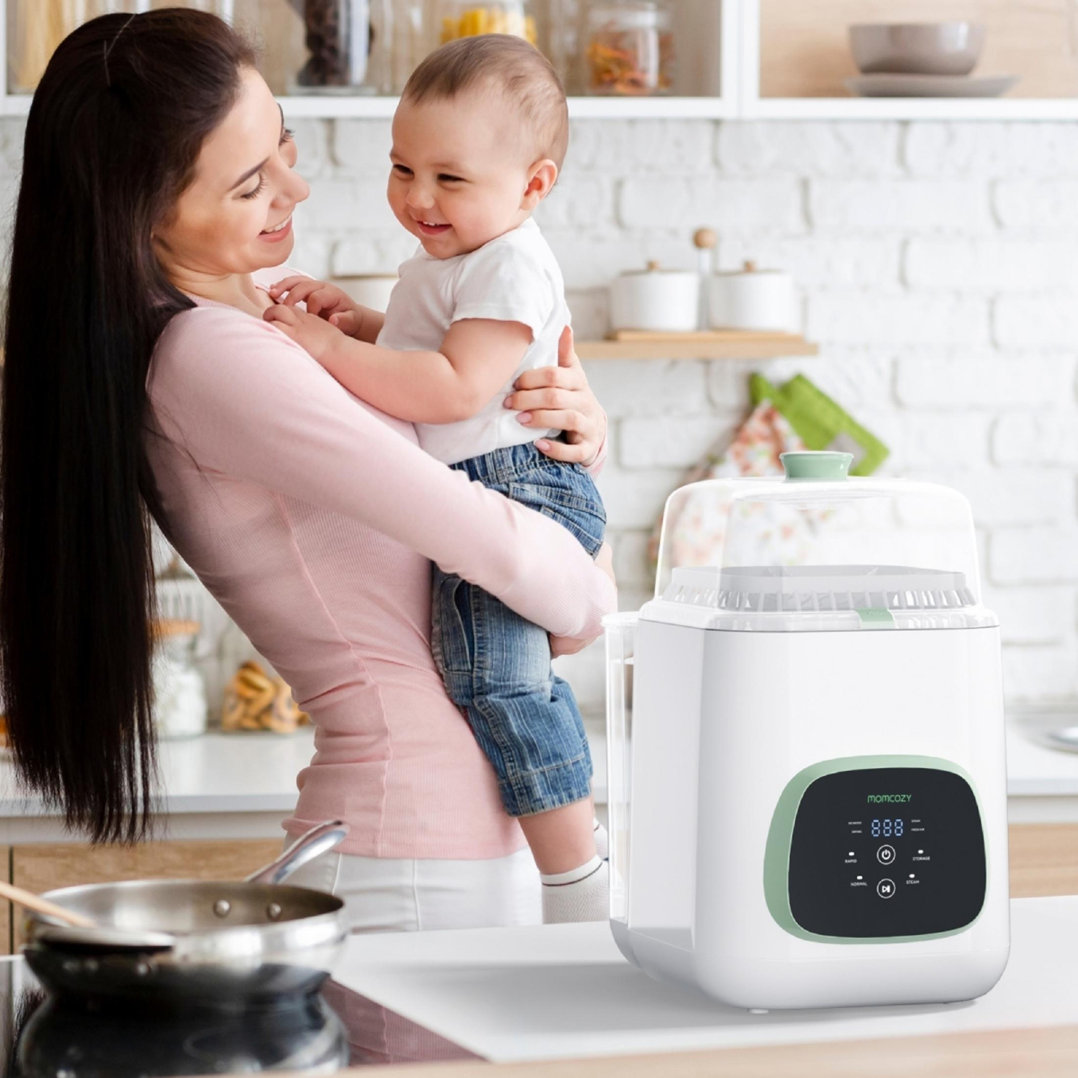 Eine Frau hält ein Baby in einer Küche. Ein Dampfgarer steht auf der Arbeitsplatte.