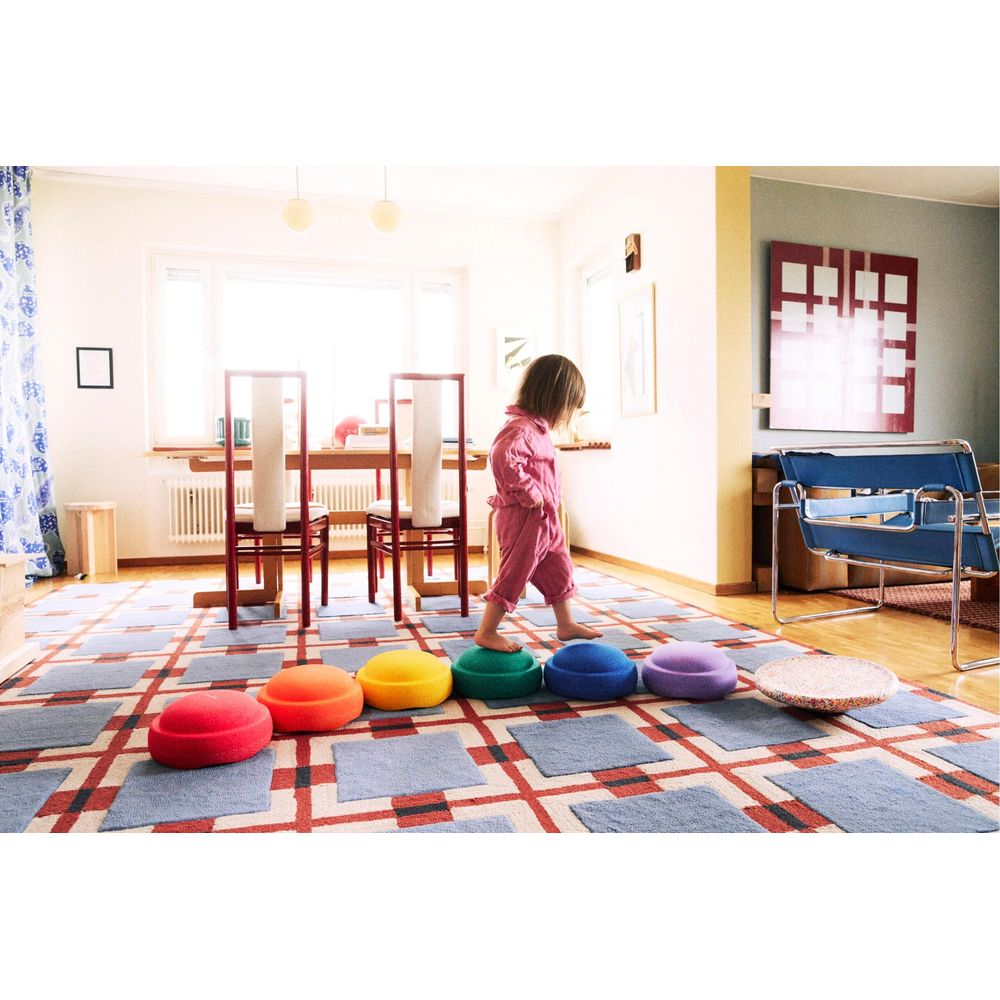 Un jeune enfant en combinaison rose se balance sur des coussins colorés sur un tapis.