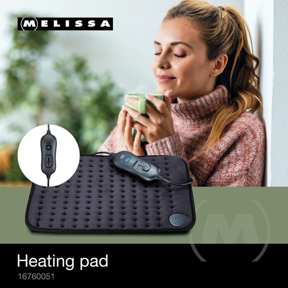 A woman drinks a hot beverage next to a black heating pad with controller.