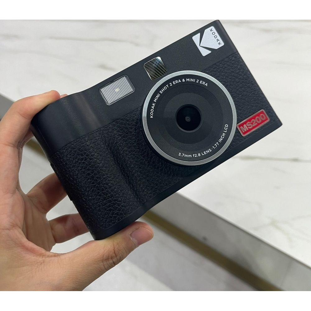 Eine schwarze Kodak Mini Shot 2 Era Sofortbildkamera mit Objektiv und Blitz, gehalten von einer Hand.