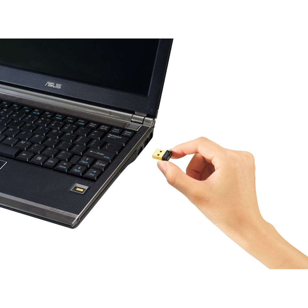 Una mano sostiene un pequeño receptor USB junto a un portátil.