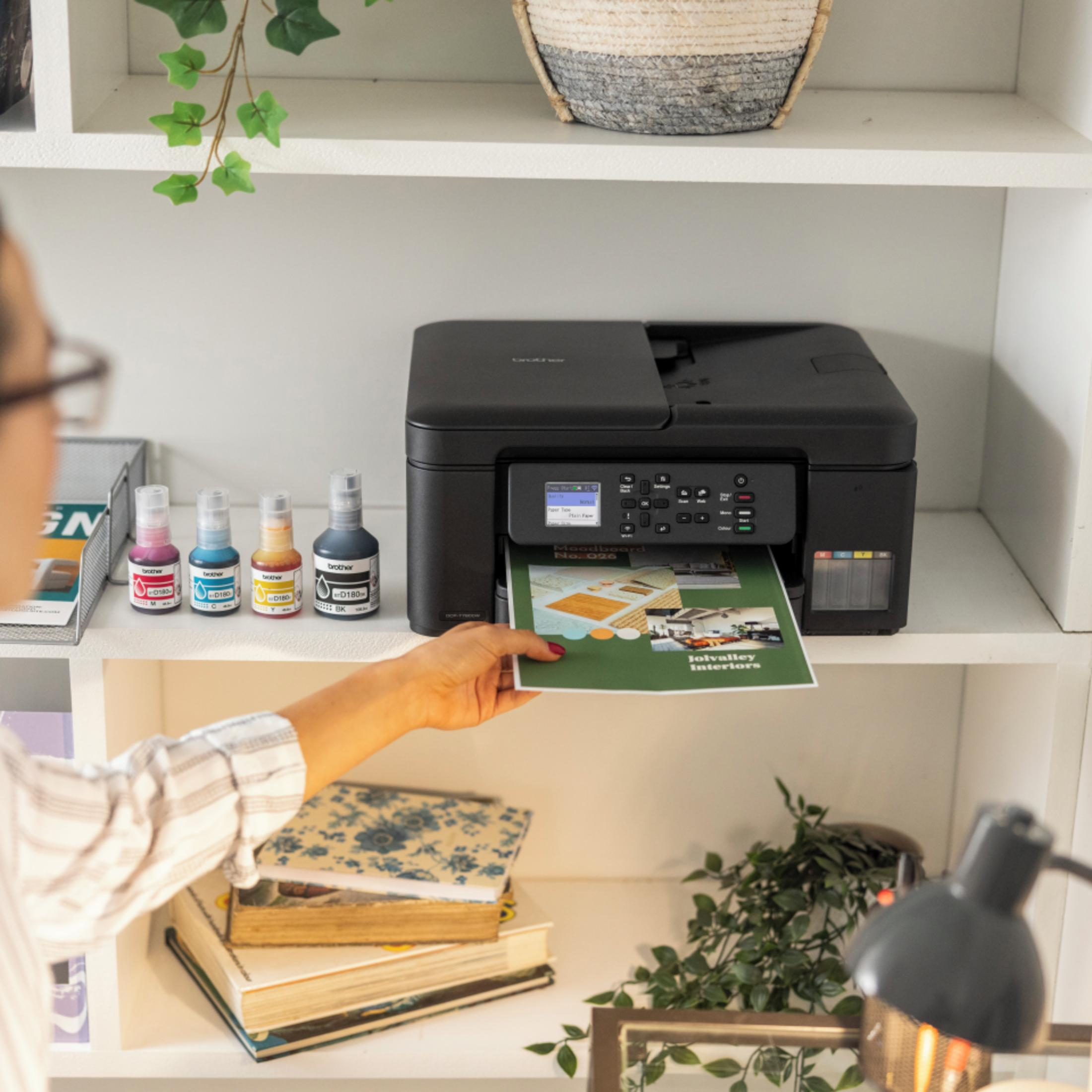 Ręka wkłada zielony arkusz do czarnej drukarki. W pobliżu butelki z tuszem.