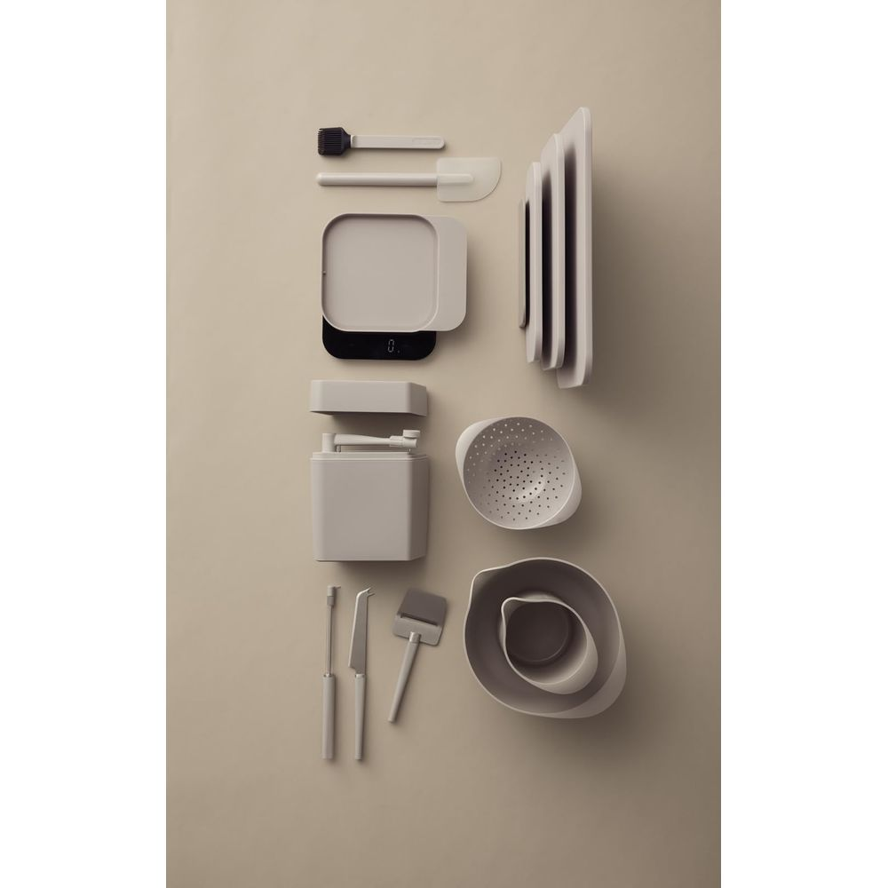 Jasnoszare przybory kuchenne ułożone na beżowym tle. Zawiera wagę, miski, deskę do krojenia.