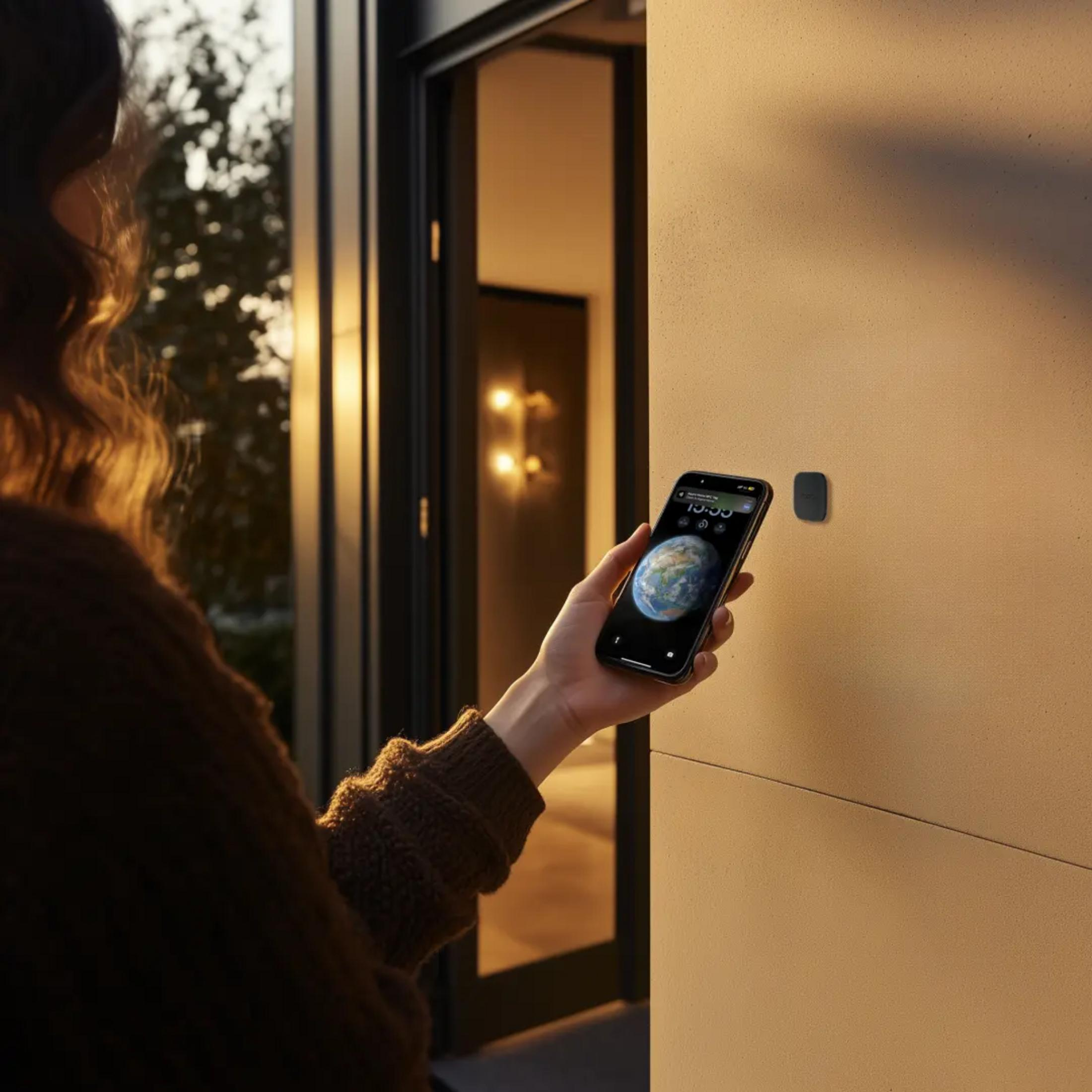 Hand hält Smartphone vor einen Wand-Sensor, Eingangsbereich.