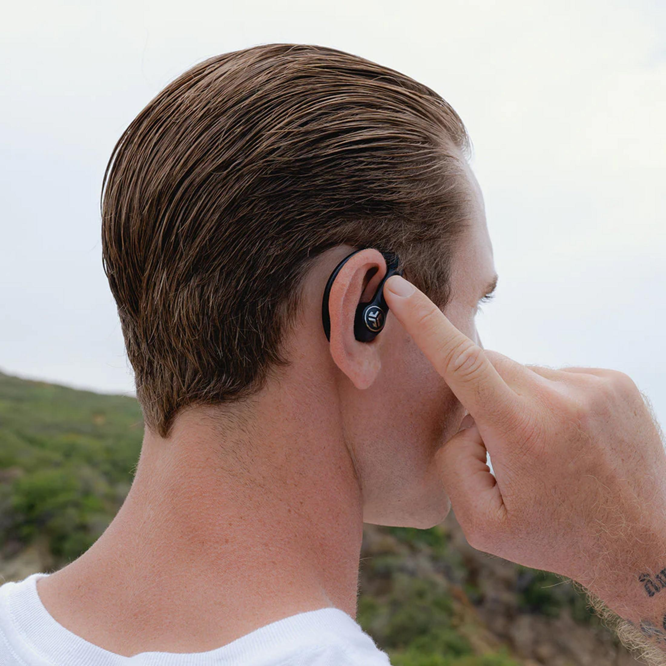 Uomo con auricolari nell'orecchio, dito che tocca l'orecchio destro. All'aperto.