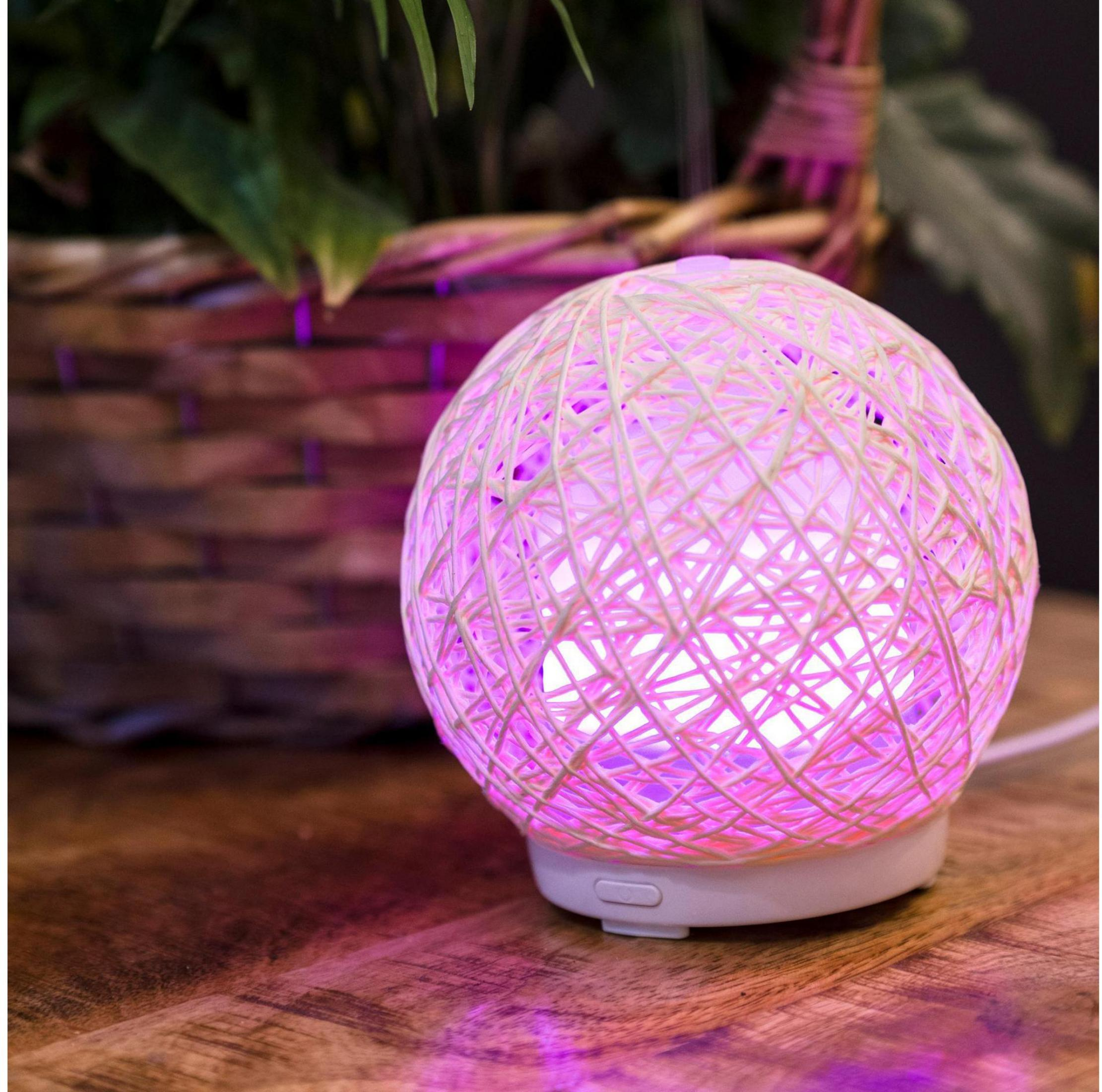 Eine kugelförmige Lampe aus weißem Garn mit rosa Licht auf einem Holztisch.