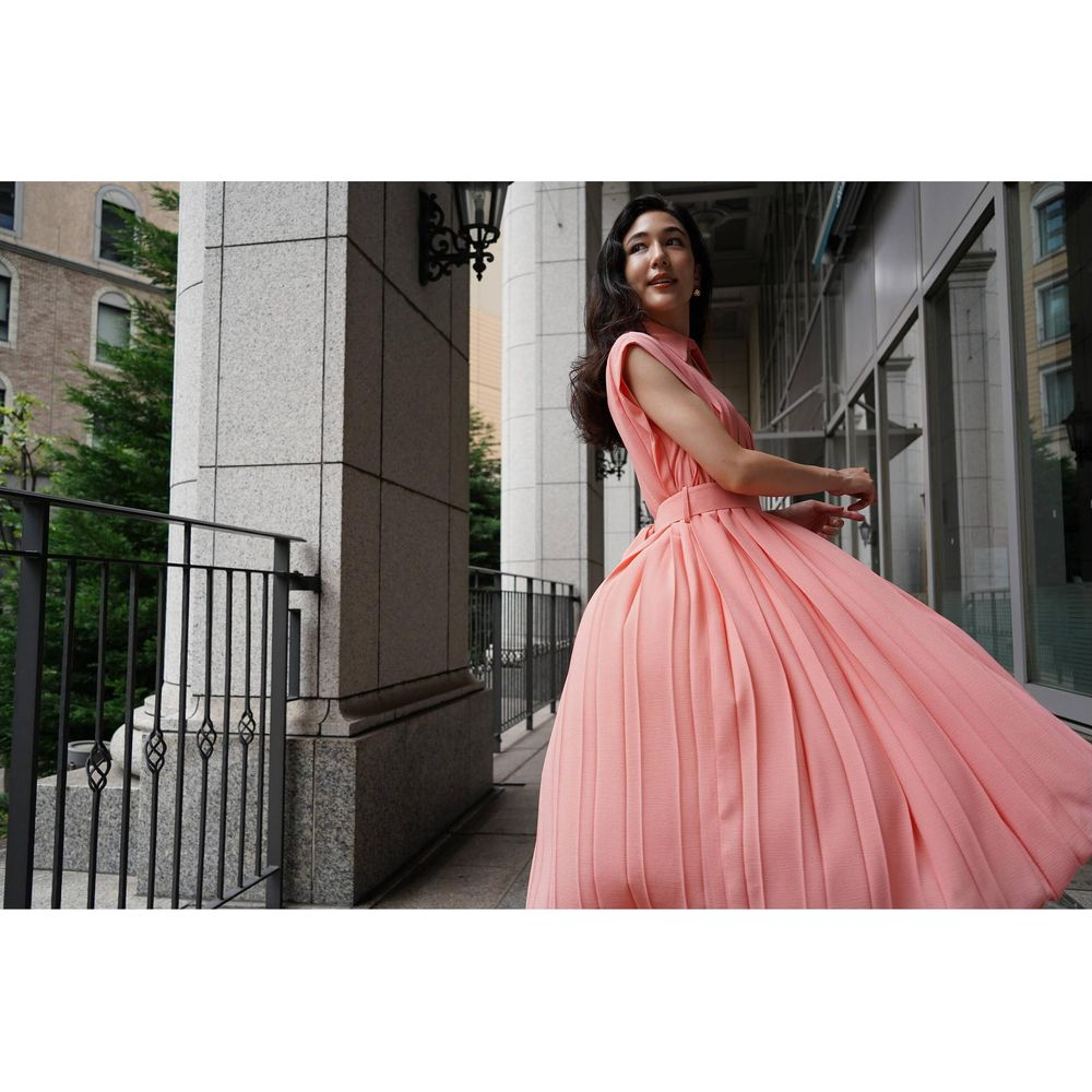 Kobieta w różowej sukience stoi na balkonie obok filaru.