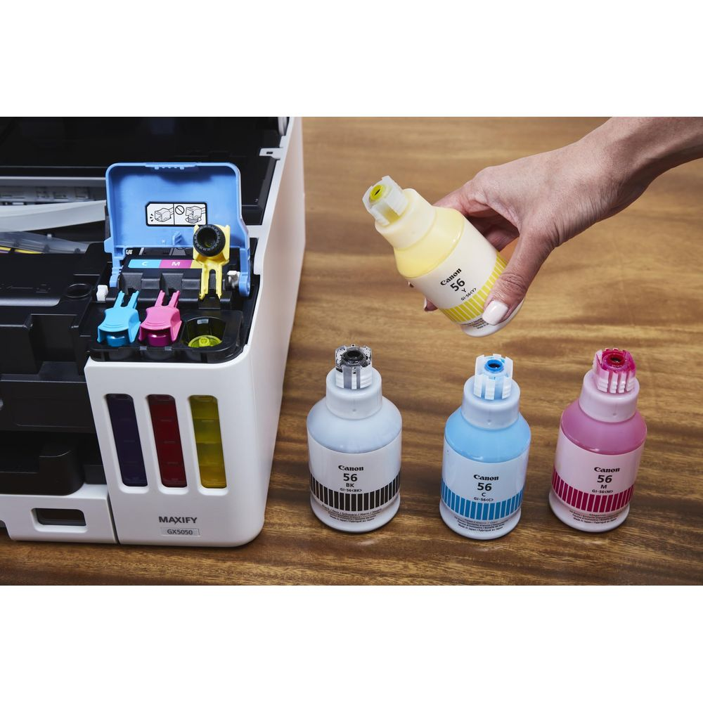 Ręka trzyma żółtą butelkę z tuszem nad drukarką z trzema innymi butelkami.