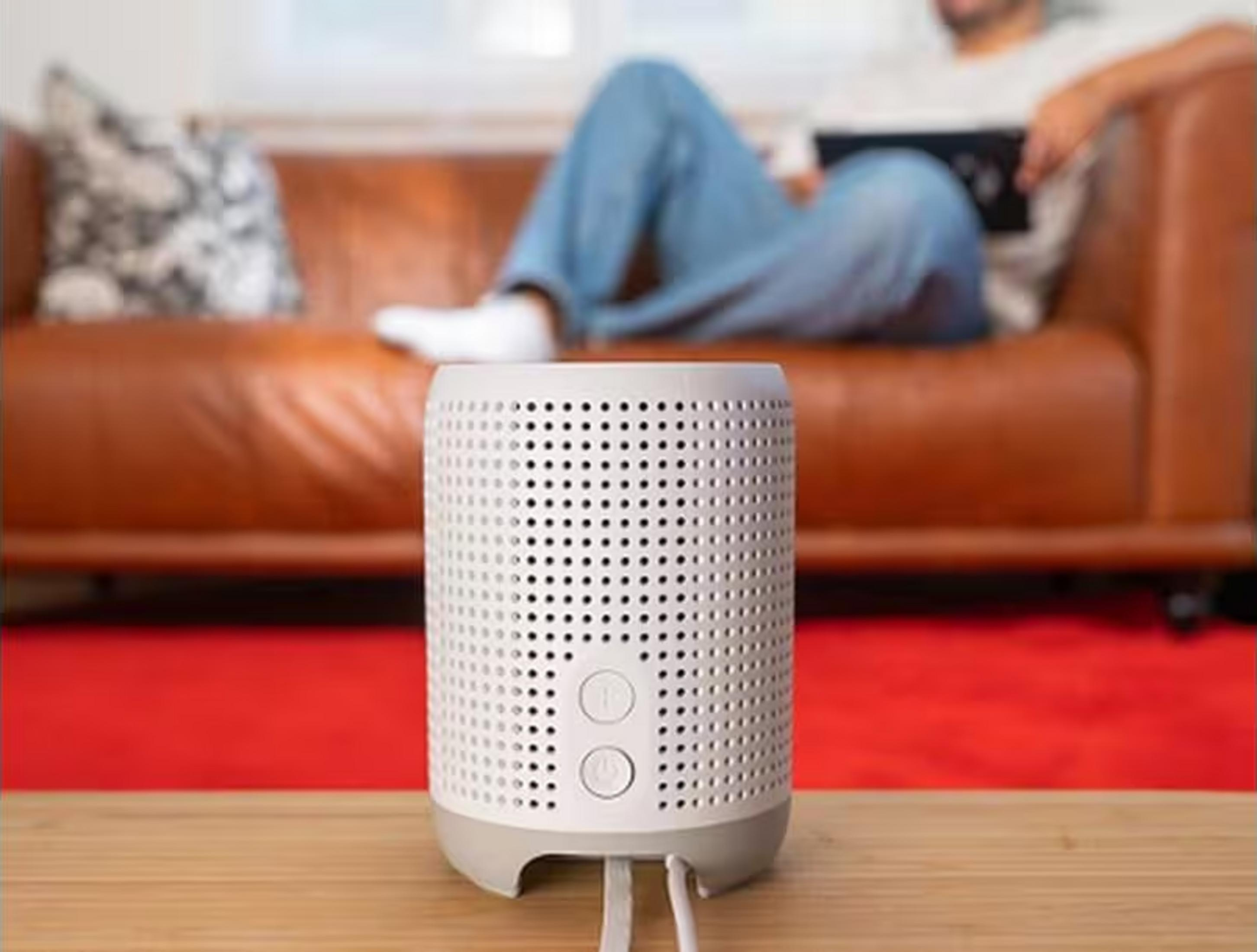 Une enceinte blanche sur une table en bois devant un homme sur un canapé.