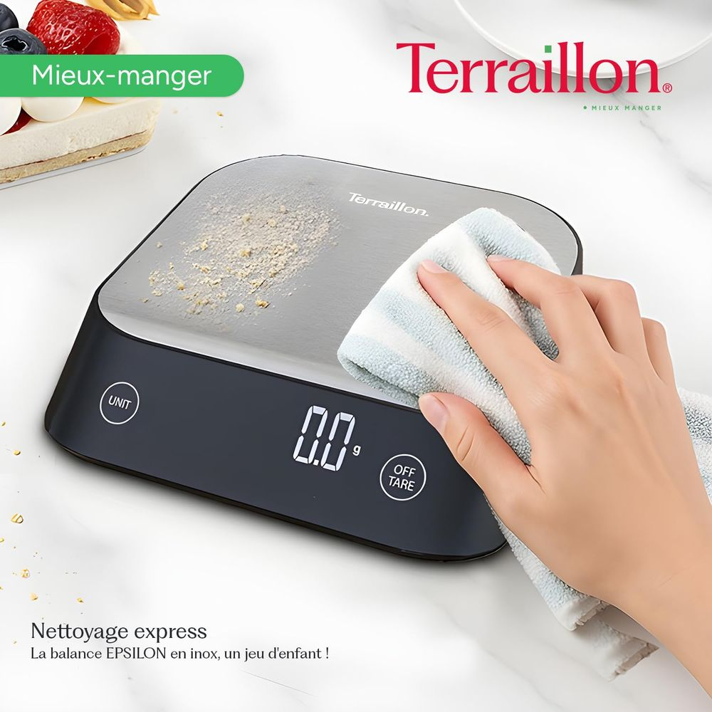 Eine Hand reinigt eine digitale Küchenwaage mit einem gestreiften Tuch. Staub liegt auf der Waage.