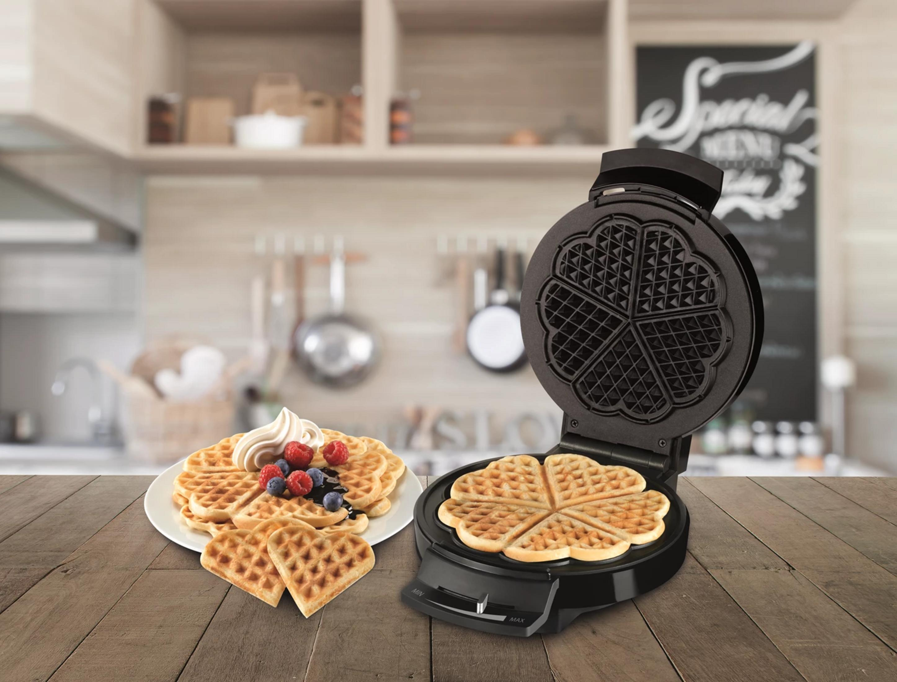 Ein offener Waffelbereiter mit Herz-Waffeln und Beeren auf einem Teller.