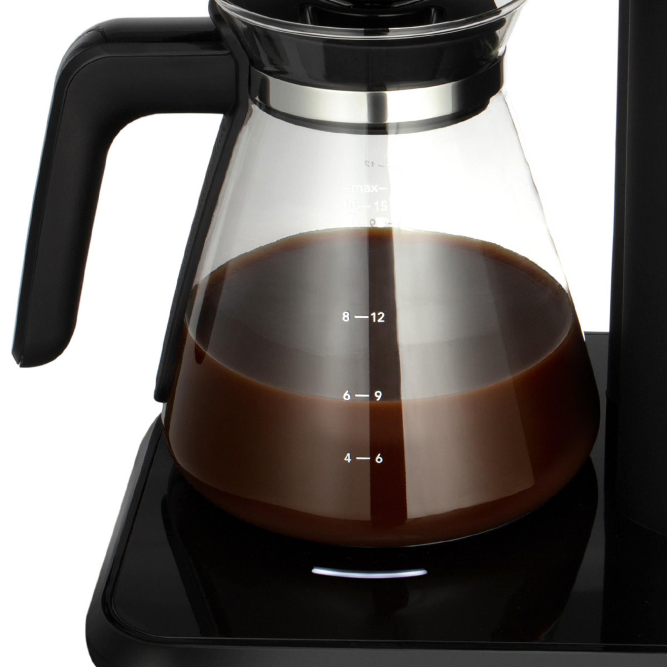 Eine schwarze Kaffeekanne aus Glas mit braunem Kaffee, auf einer schwarzen Basis.