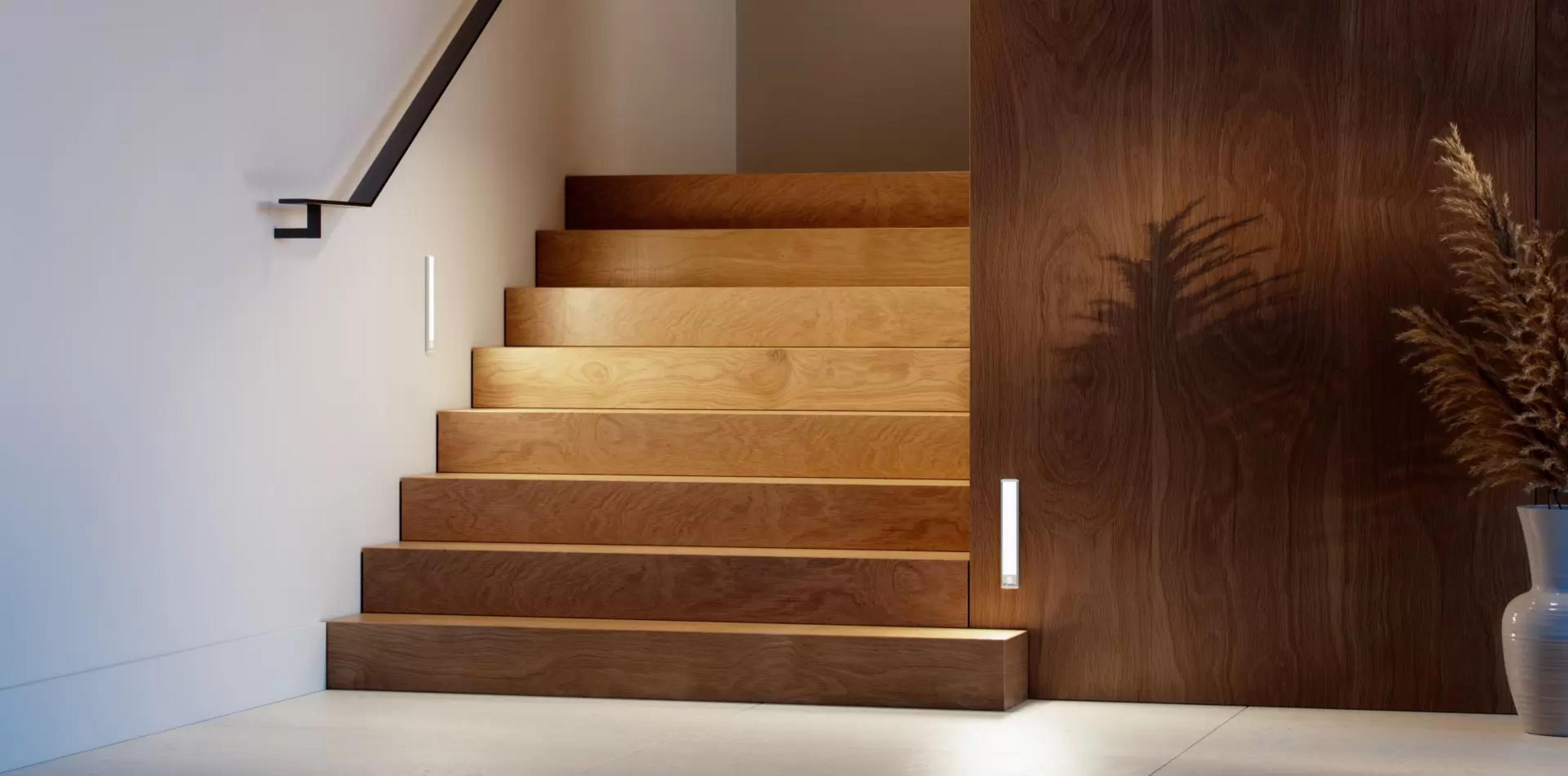 Eine Holztreppe mit schwarzem Geländer und Wandleuchten daneben.