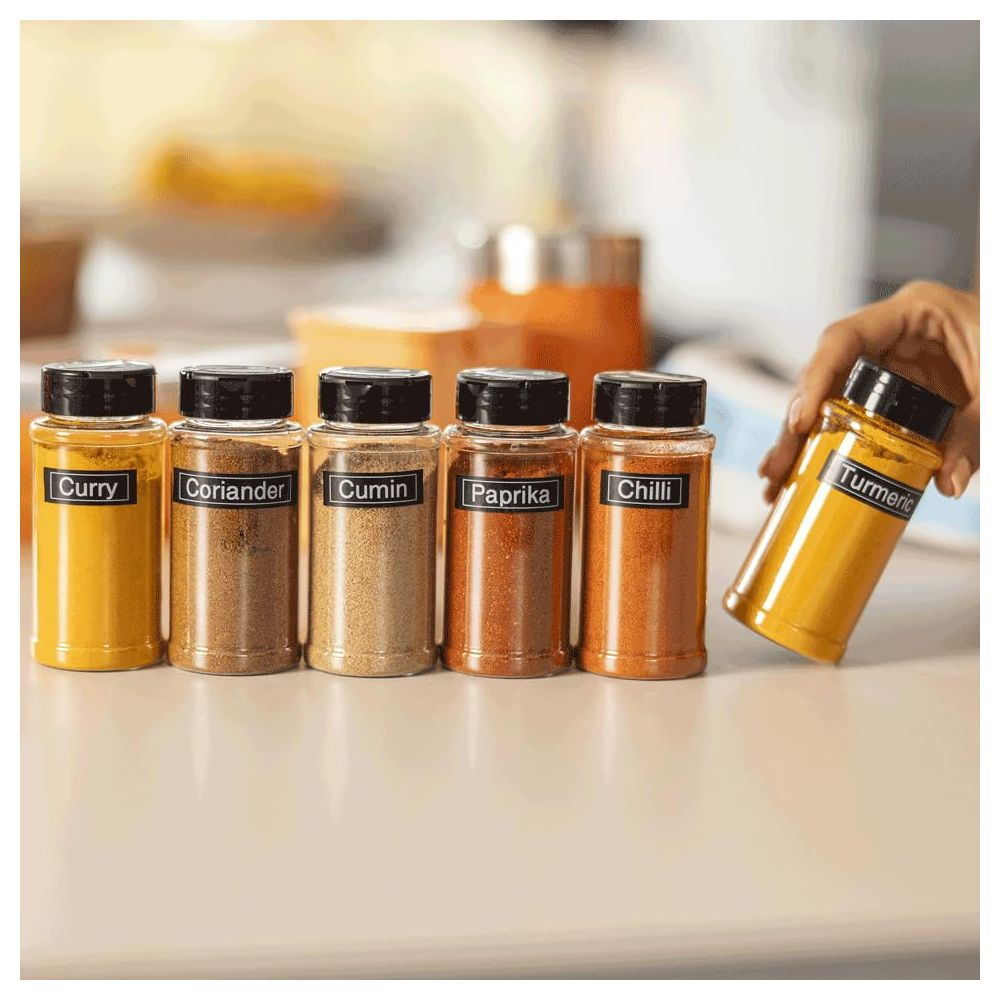 Sześć słoików z przyprawami na stole, jeden trzymany przez rękę.