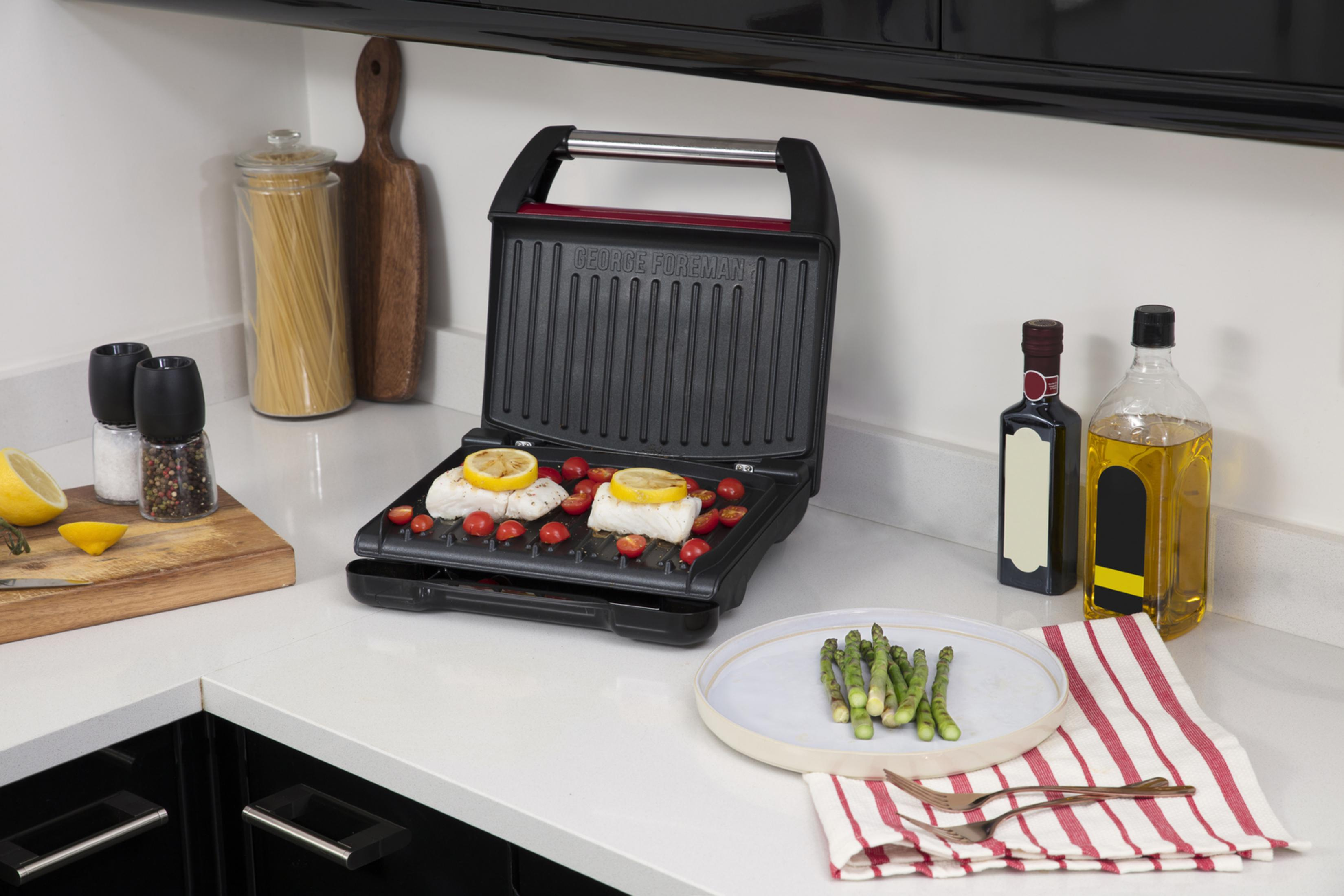 Una griglia George Foreman con pesce, limone e pomodori. Asparagi e condimenti nelle vicinanze.