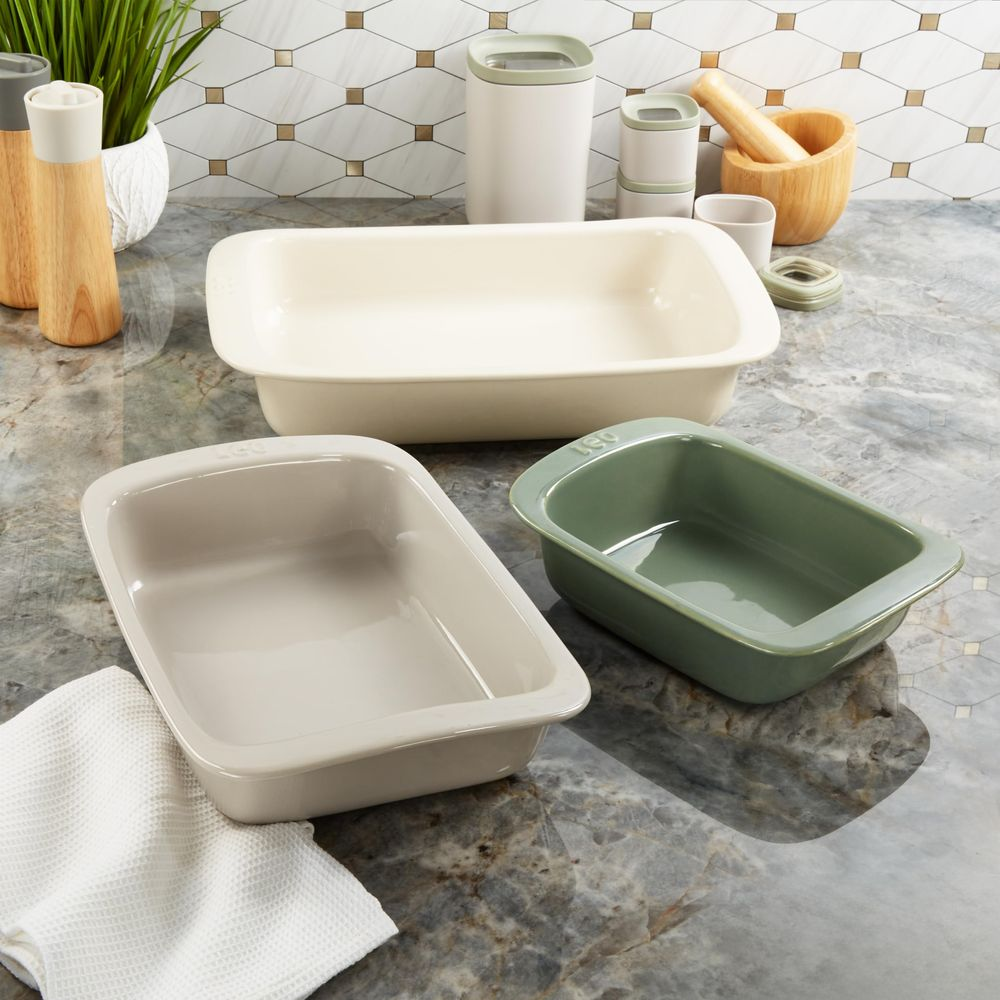Trzy ceramiczne naczynia do pieczenia w kolorze kremowym, szarym i zielonym na marmurowym blacie.