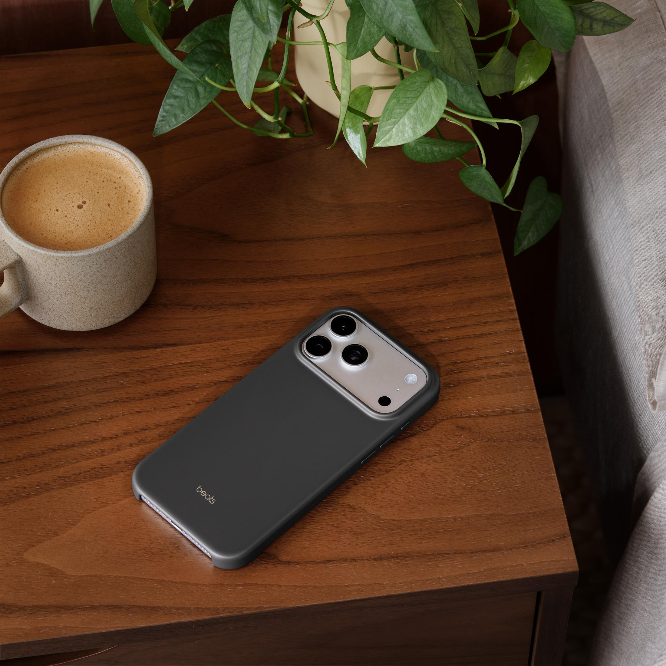 Un teléfono negro descansa sobre una mesa de madera junto a una taza de café y una planta.
