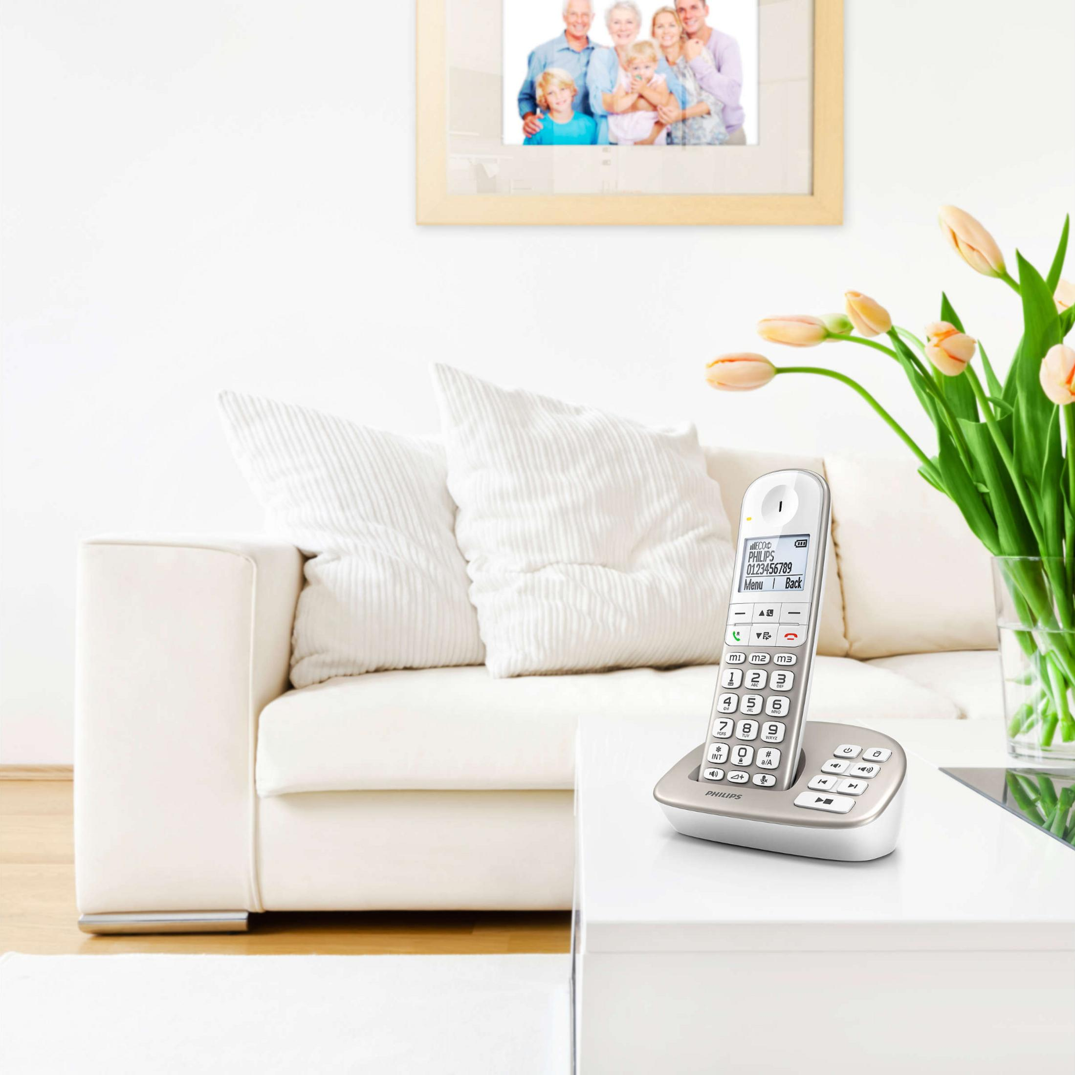 Ein weißes schnurloses Telefon steht auf einem weißen Tisch neben einer Vase mit Tulpen.