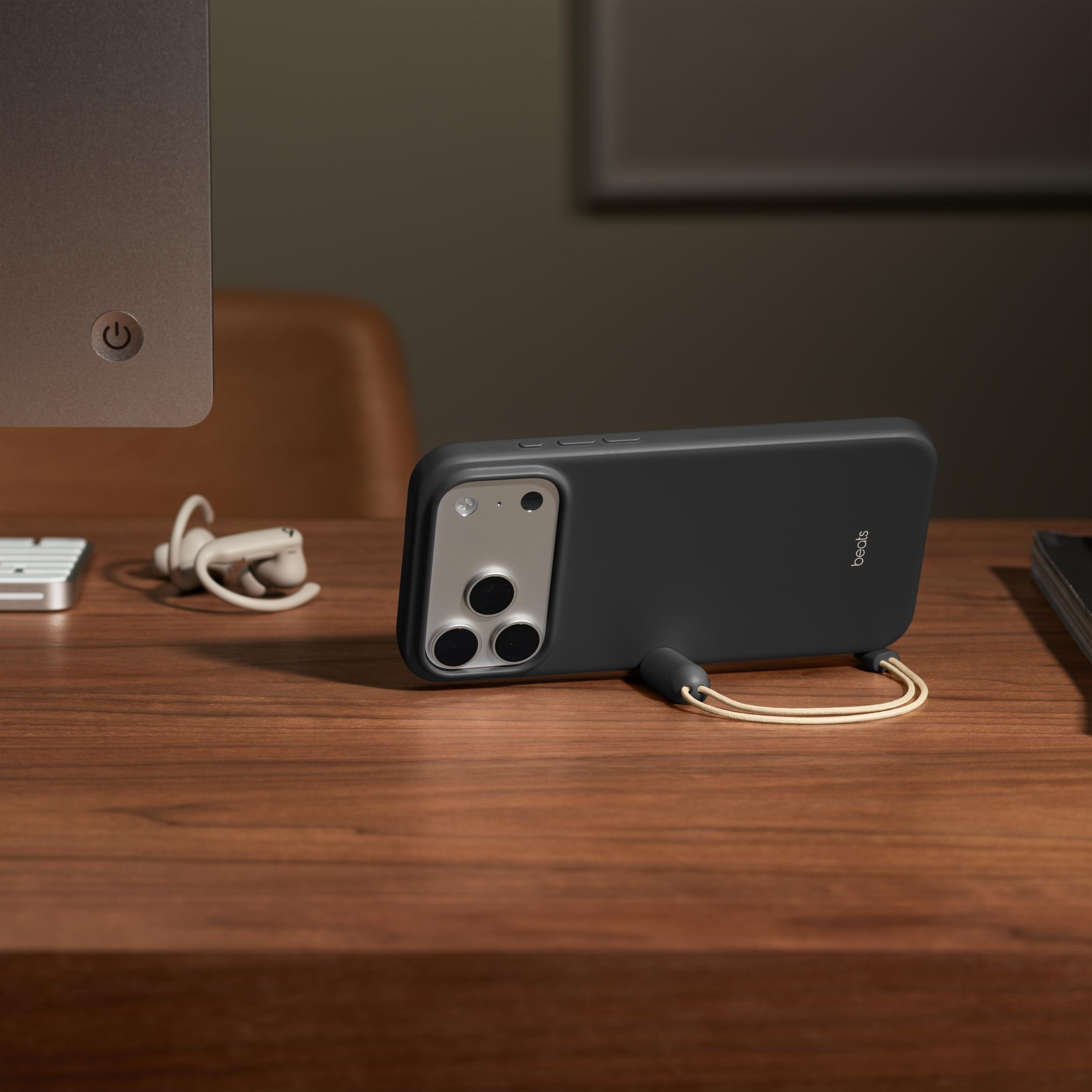 Czarny iPhone w etui Beats leży na drewnianym biurku obok słuchawek.