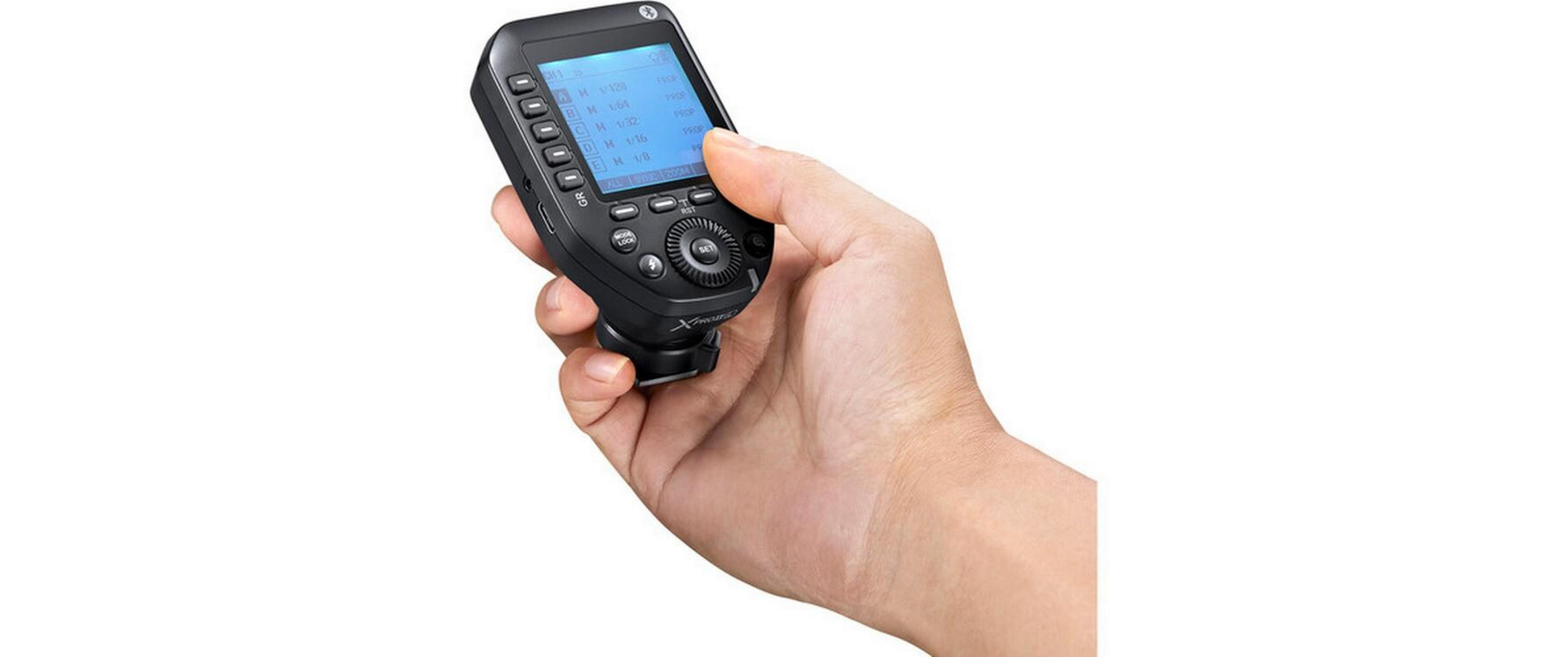 Una mano tiene un controller flash per fotocamera nero con schermo blu.