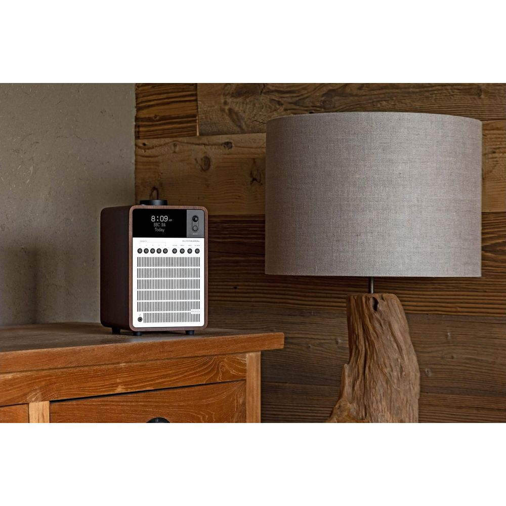 Een bruine digitale radio staat op houten meubels naast een lamp met grijze kap.