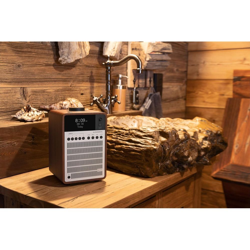 Een bruine radio staat op een houten aanrecht, met een rustiek wastafel en kraan erachter.