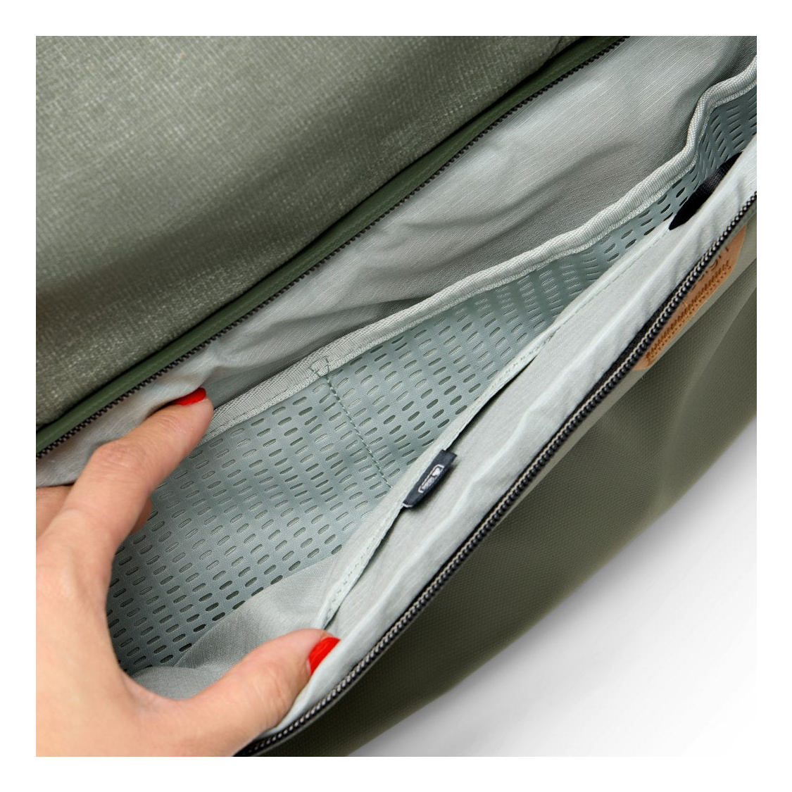 A hand with red nails touches an olive green mesh pocket inside a bag.