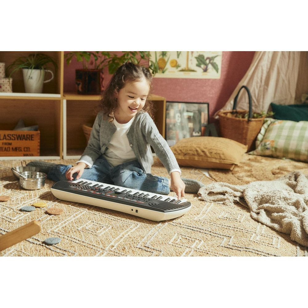 Ein kleines Mädchen spielt auf einem Keyboard, das auf einem Teppich liegt.
