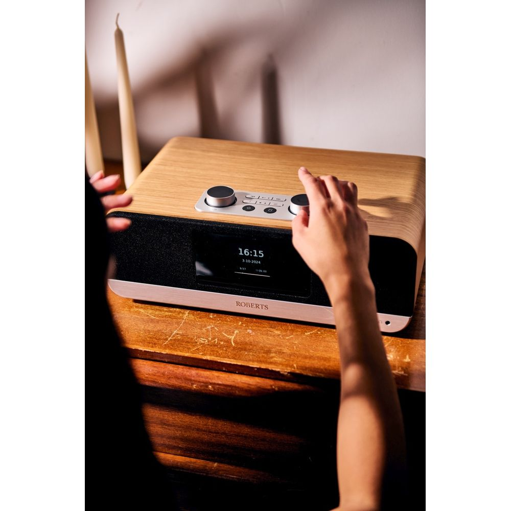 Una mano regola una radio in legno con altoparlante e schermo neri. Due candele dietro.