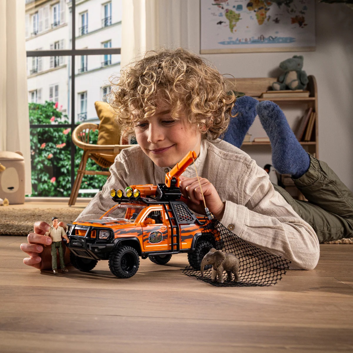 Ein Junge spielt mit einem orangen Spielzeug-Jeep mit Tigermuster, einer Figur und einem Elefanten.