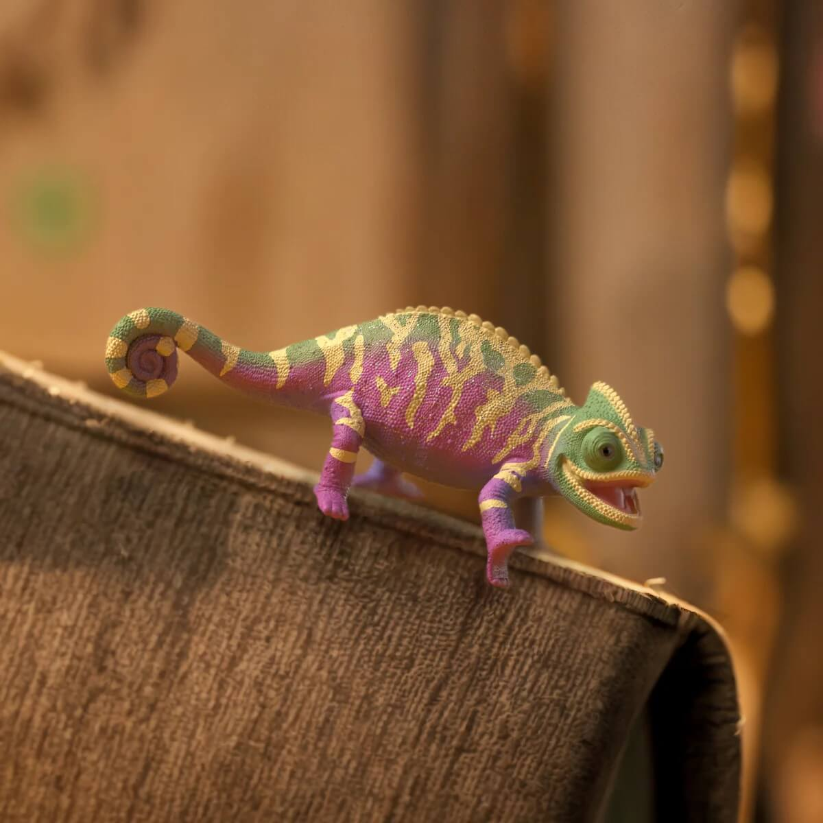 Un caméléon jouet coloré avec des taches violettes et jaunes sur du tissu marron.