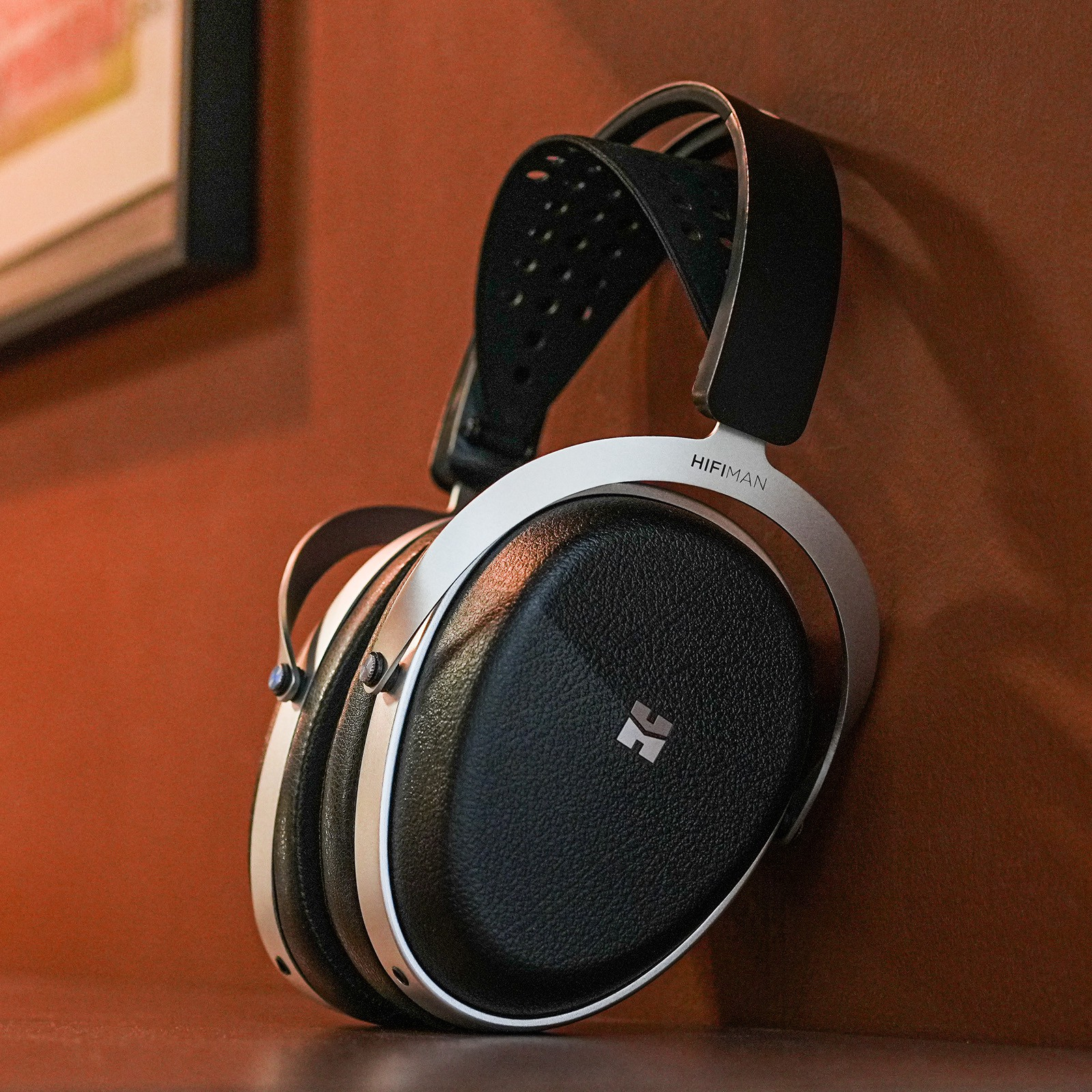 Cuffie Hifiman nere con archetto argentato appese a un muro marrone.