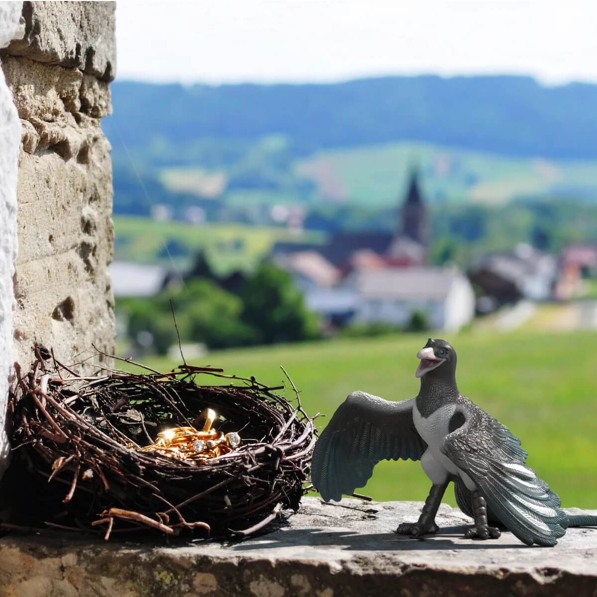 Ein Vogelspielzeug neben einem Nest mit glänzenden Objekten, Dorf im Hintergrund.