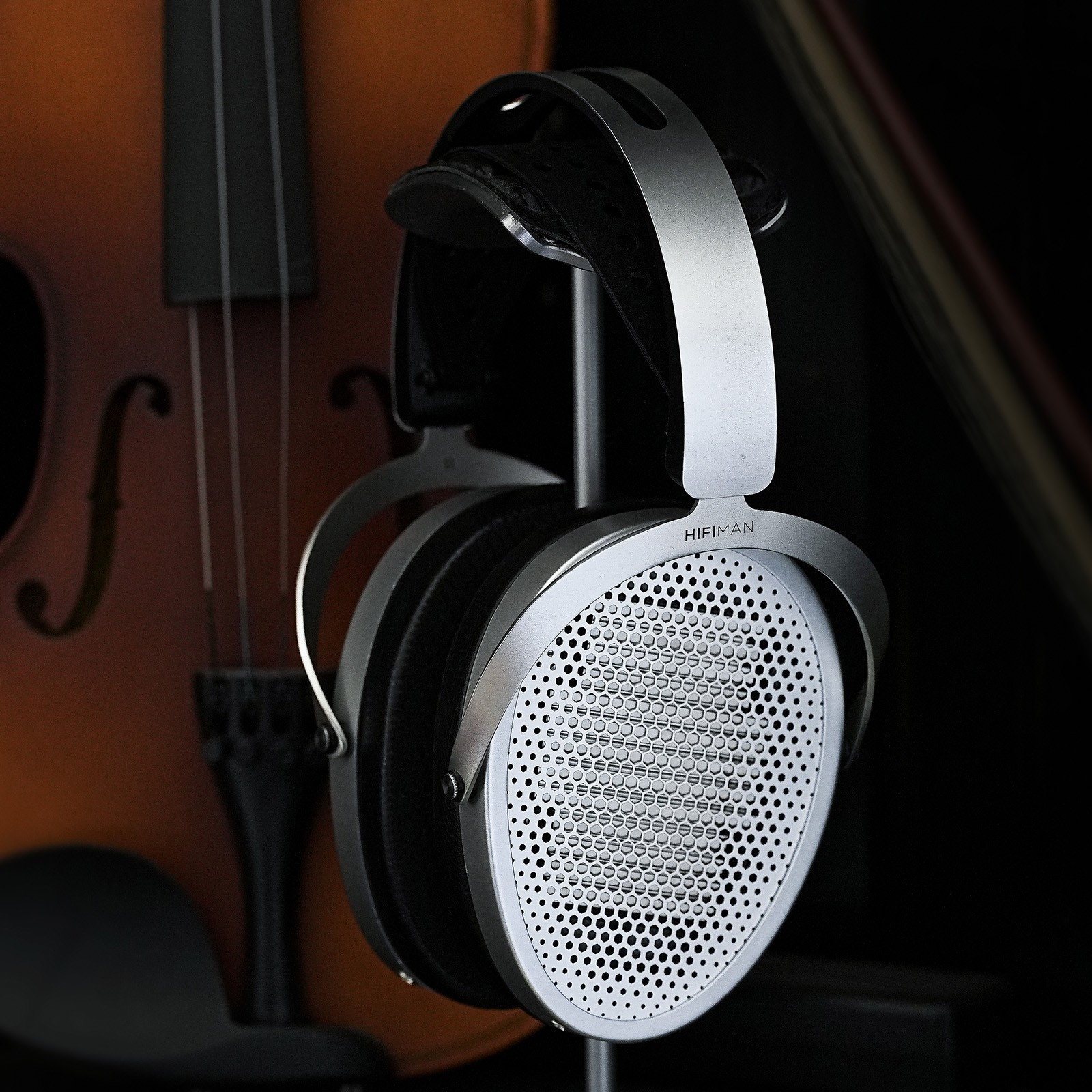 Cuffie argentate pendono davanti a un violino. Sfondo scuro.