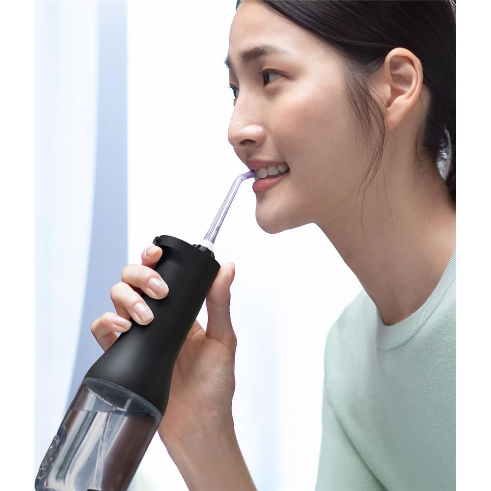 Una donna usa un irrigatore orale nero con serbatoio dell'acqua trasparente.