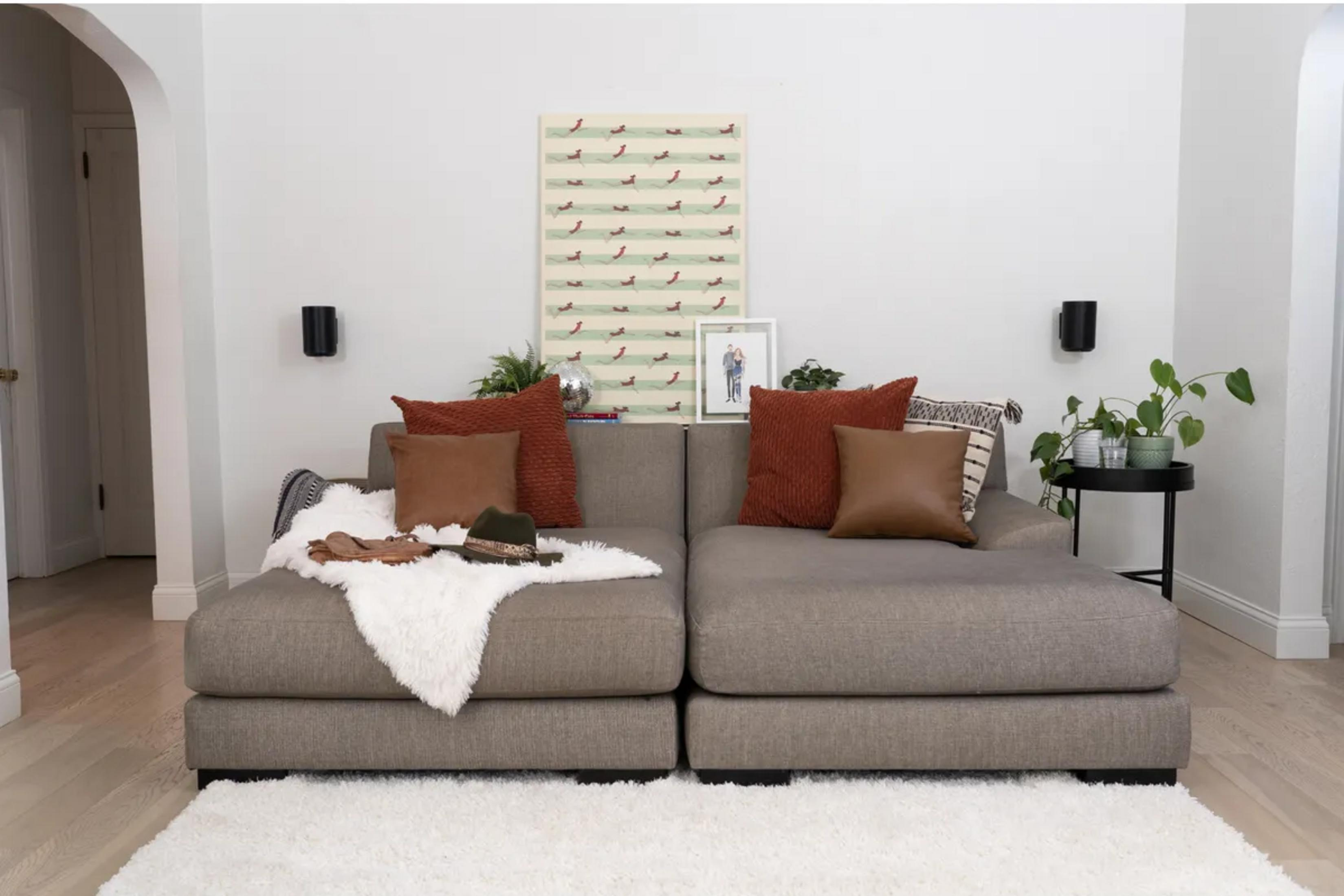 A gray sectional sofa with pillows, a throw, and a hat. Wall art and plants are visible.