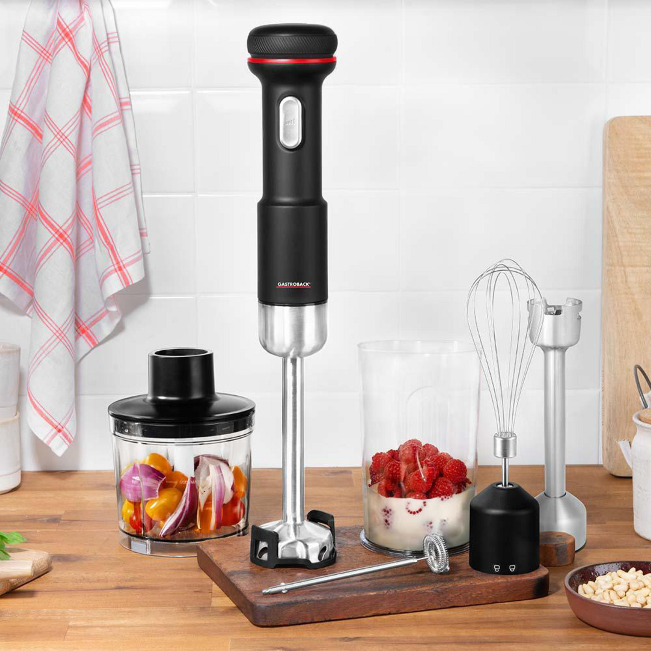 Ein Stabmixer mit Zubehör, Beeren und Gemüse auf einem Holztisch.