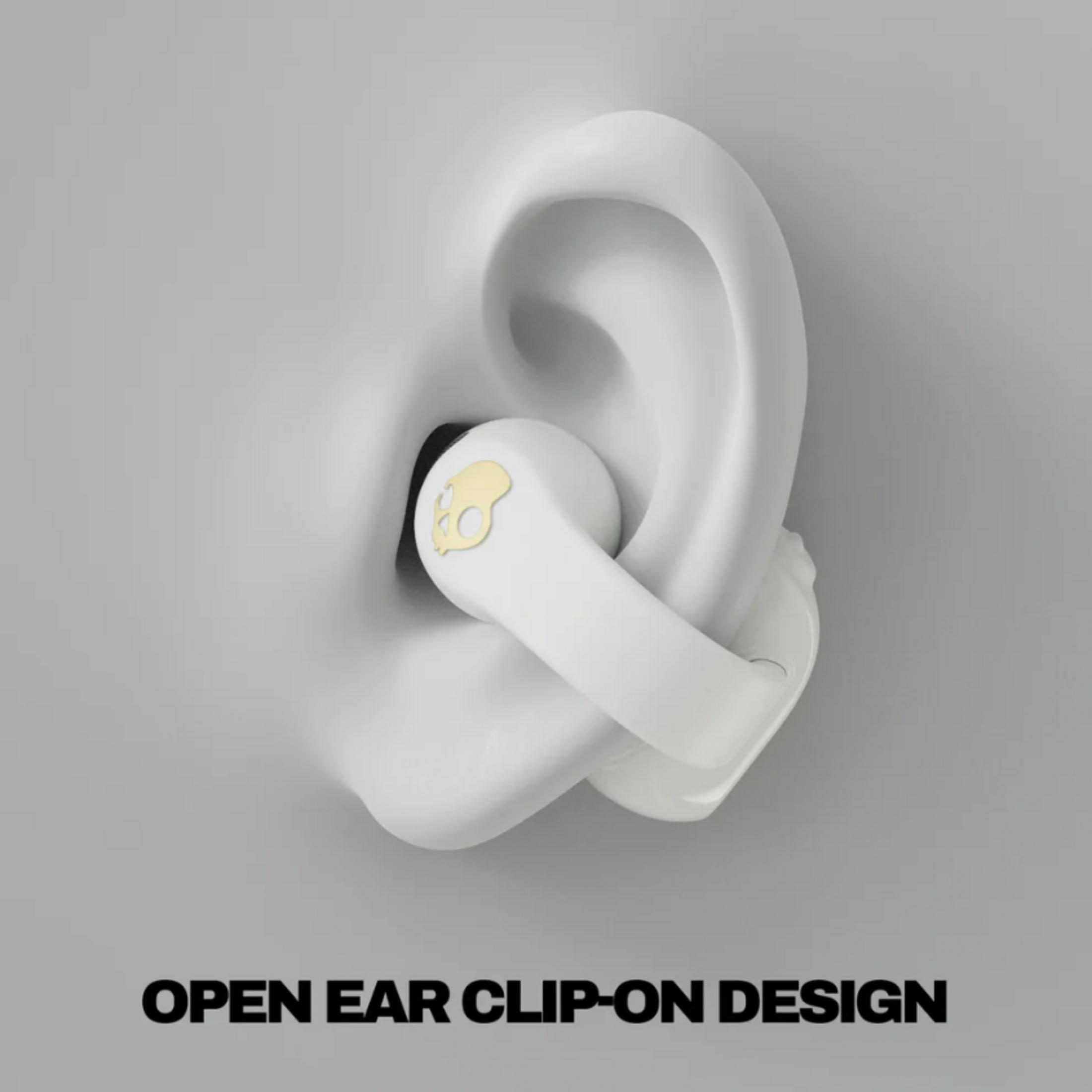 Un auricolare bianco con logo teschio dorato poggia in un orecchio bianco stilizzato.
