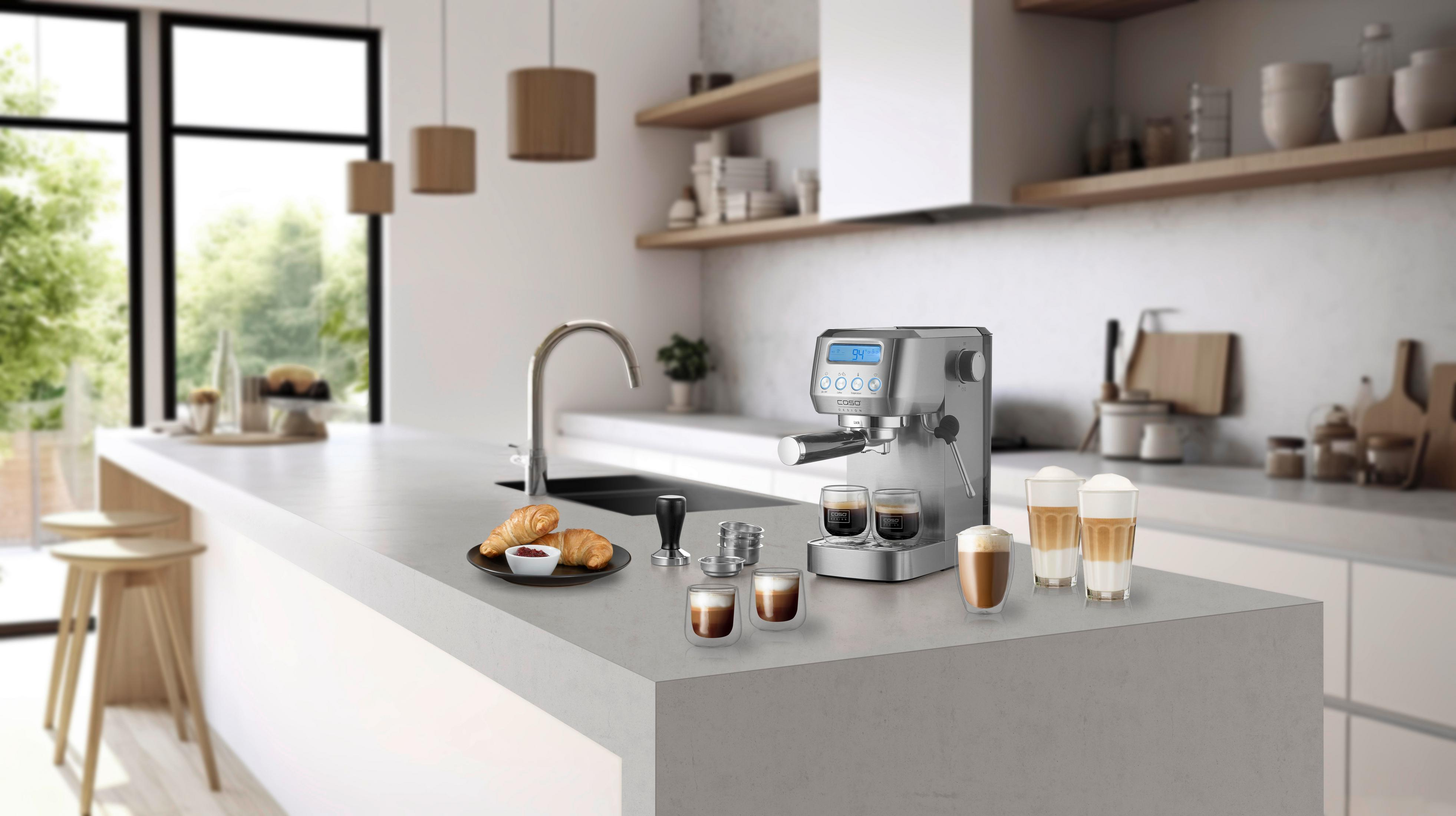 Silberne Kaffeemaschine mit fertigen Kaffees und Croissants auf einer Küchenarbeitsplatte.