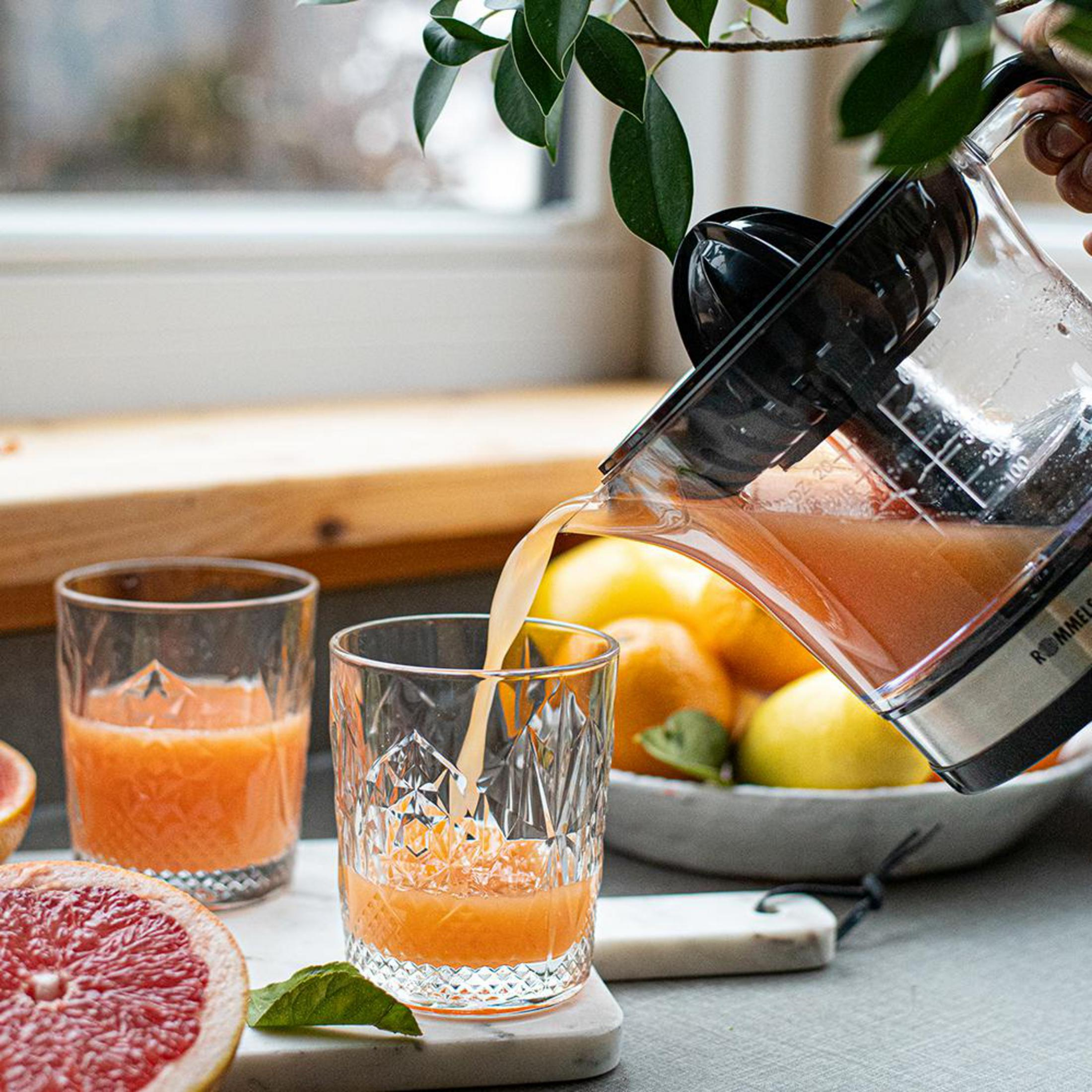 Saft wird aus einem Krug in ein Glas gegossen, daneben Grapefruits und Zitronen.