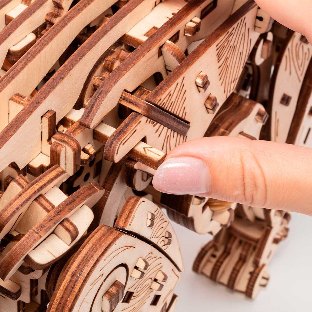 Eine Hand setzt ein Holzteil in ein mechanisches Modell ein.