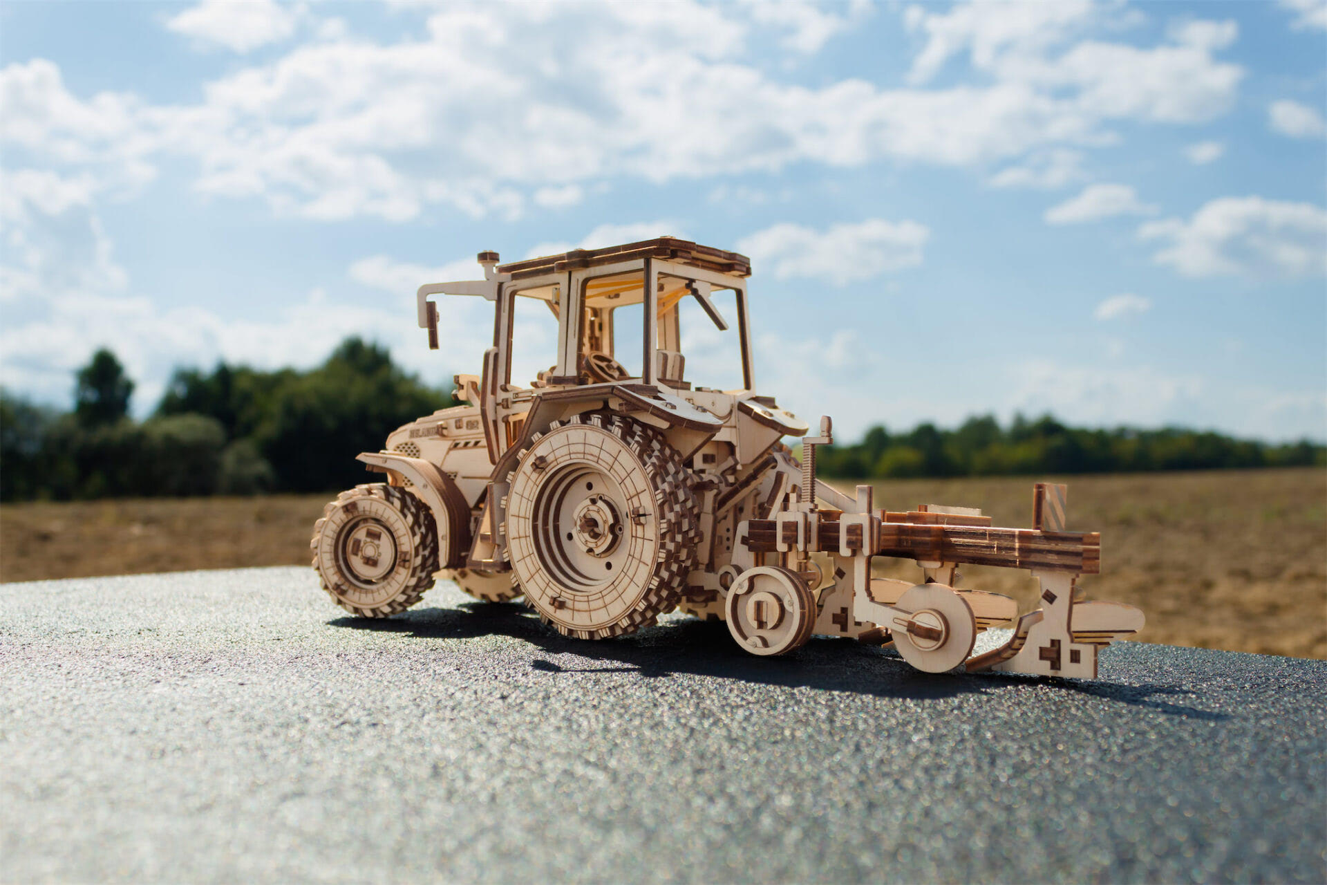 Ein hölzernes Modell eines Traktors mit angehängtem Pflug steht auf einer Oberfläche.