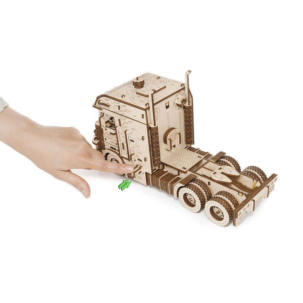 Ein Holzmodell-LKW wird von einer Hand mit einem grünen Pfeil berührt.