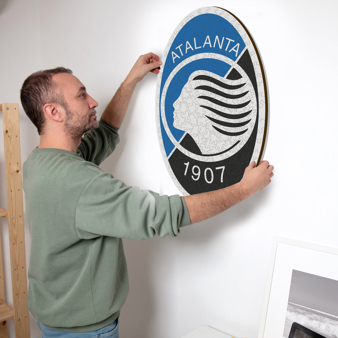 Mann hängt Atalanta-Logo-Puzzle mit der Zahl 1907 an die Wand.