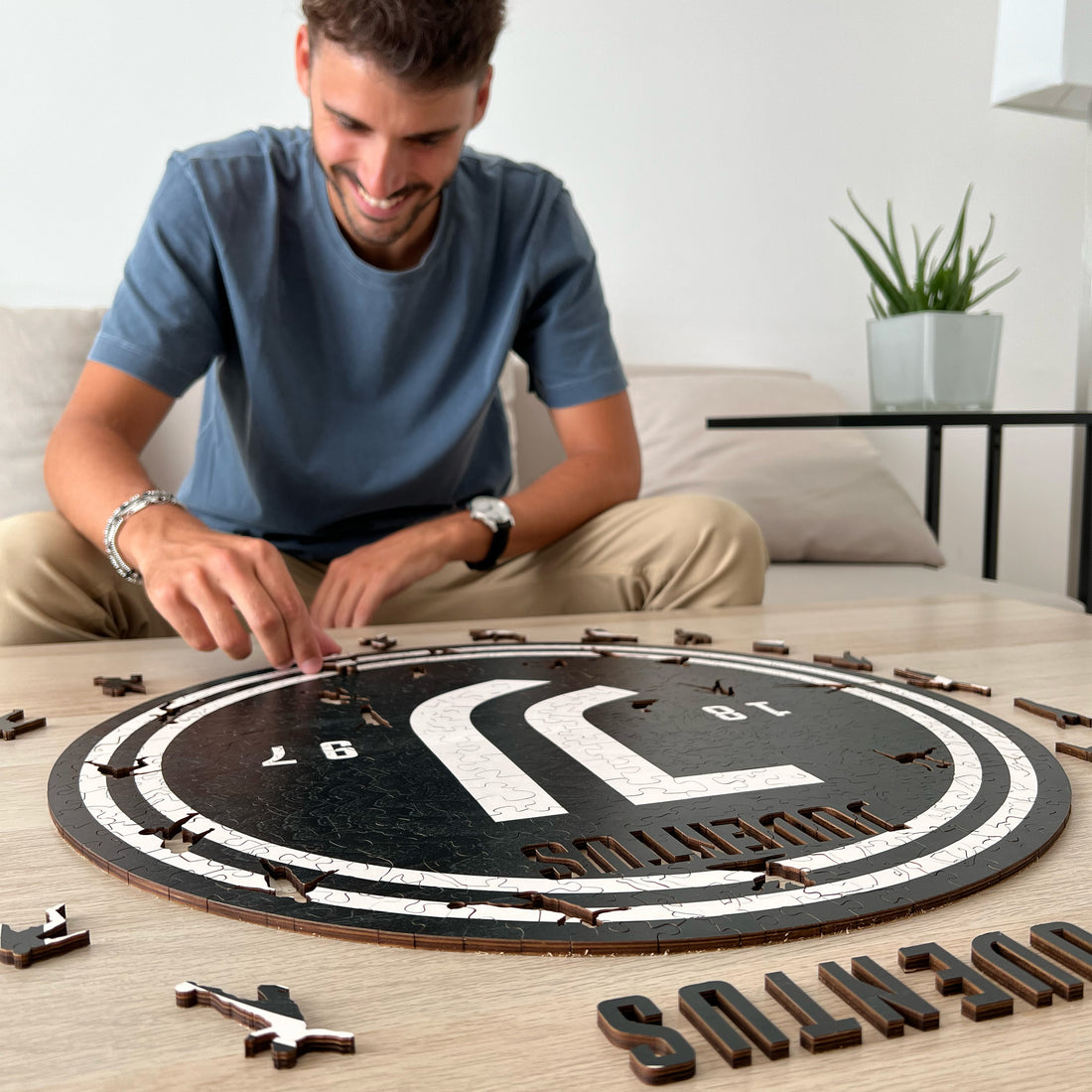 Mann baut ein Juventus-Puzzle auf einem Holztisch. Er trägt ein blaues T-Shirt.