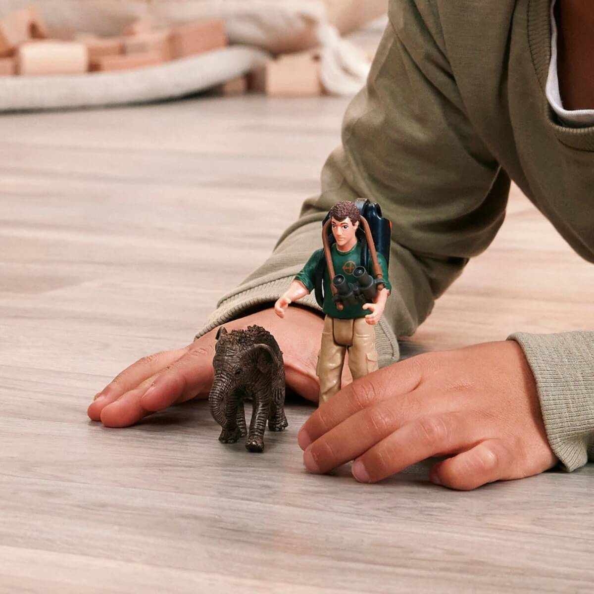 Un bambino gioca con una figura di elefante e una figura di esploratore su un pavimento di legno.