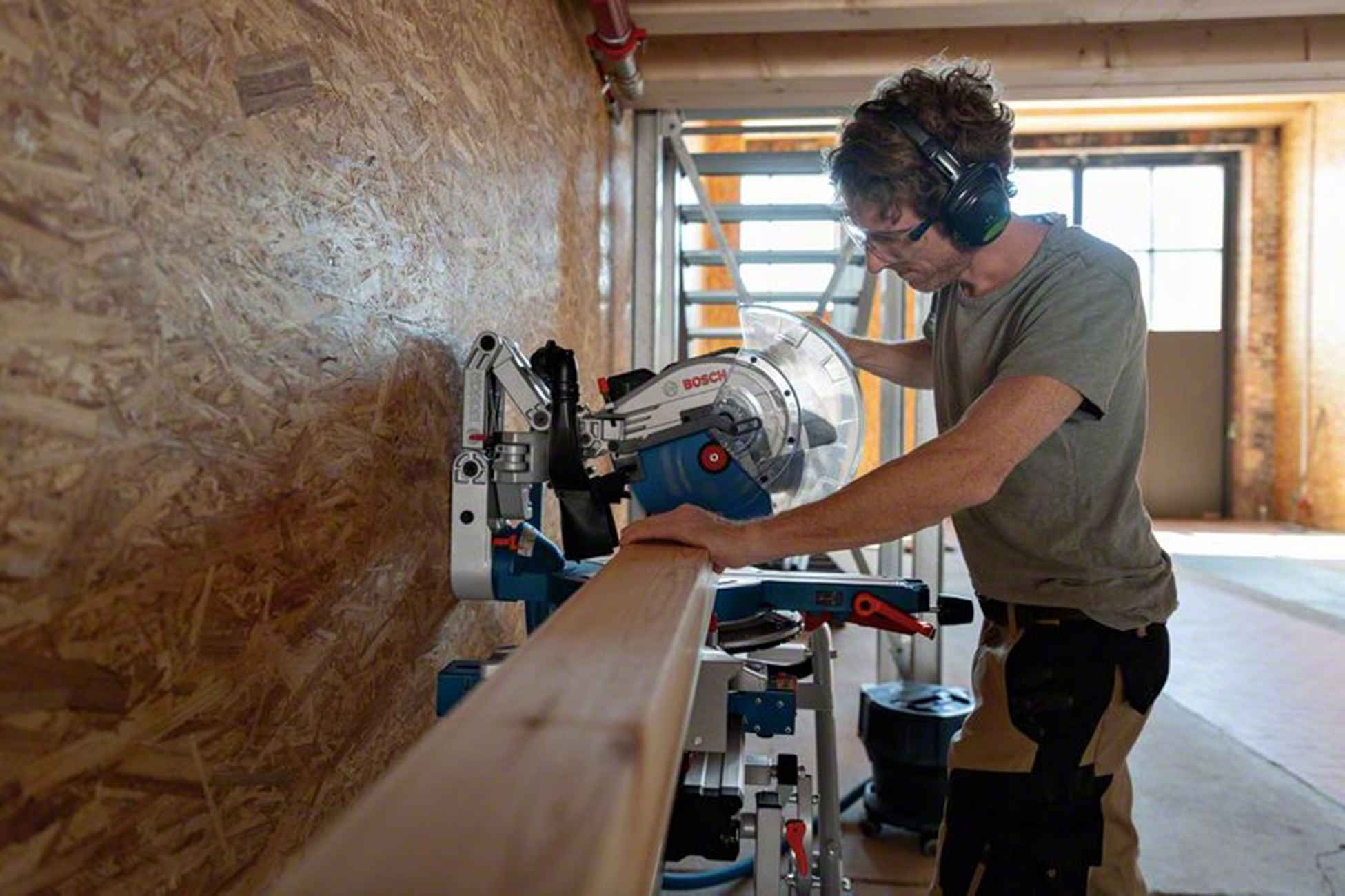 Mann mit Schutzbrille und Kopfhörern schneidet Holz mit einer Kreissäge.